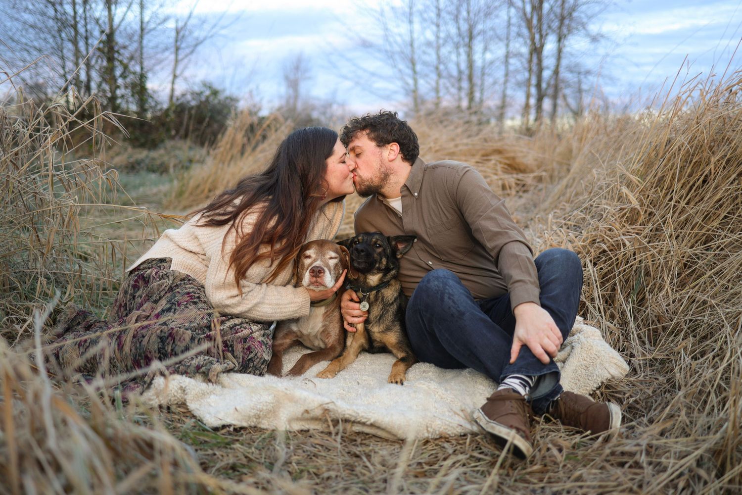 Romantic couple sharing tender moments on a blanket in a field during golden hour.
