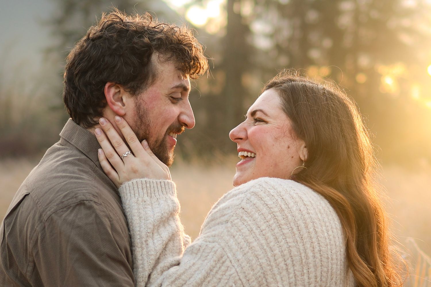 Couple laughing and embracing outdoors during sunset with warm lighting.
