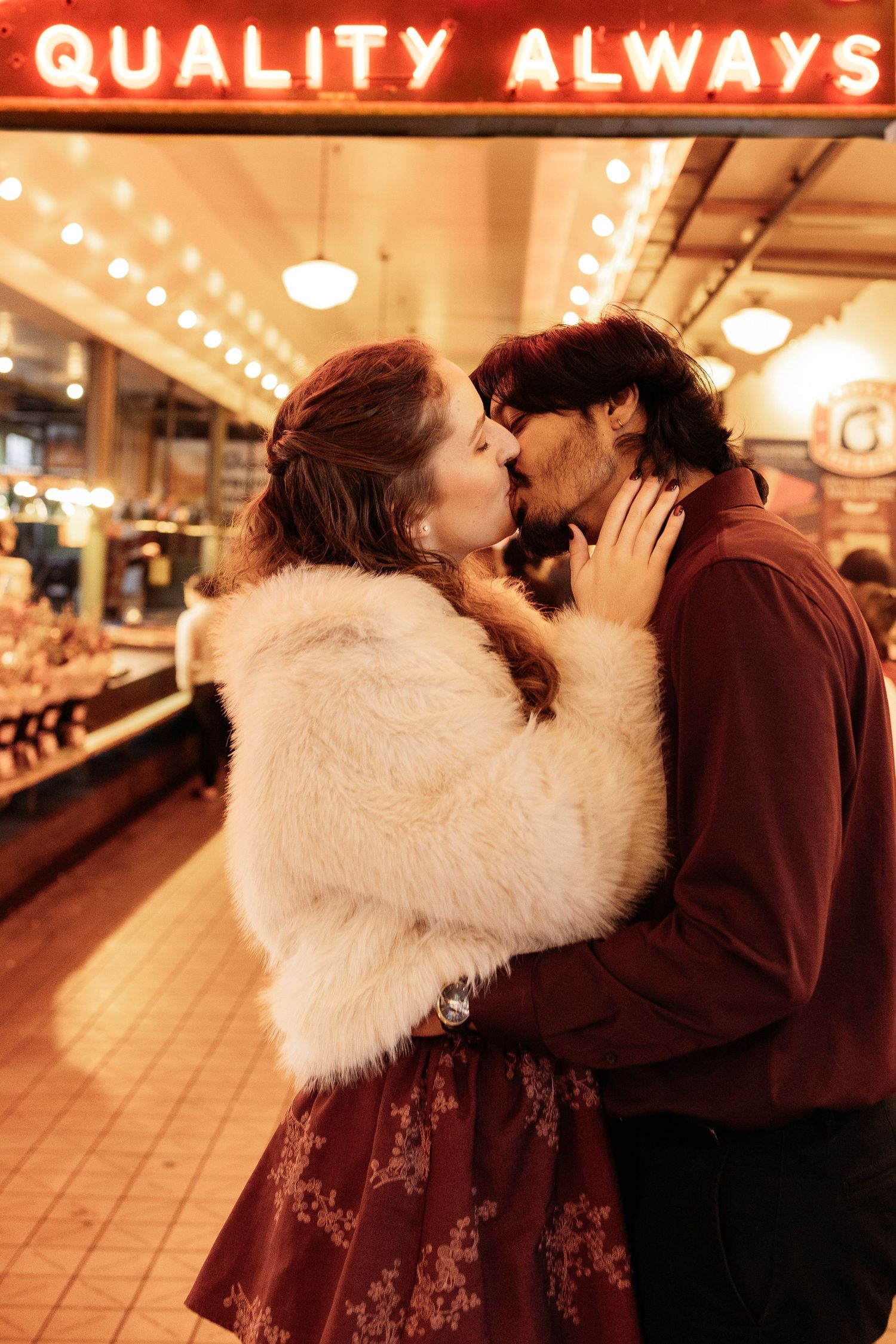 A couple shares a romantic kiss in a vintage-style bowling alley with warm lighting and retro decor in the background.