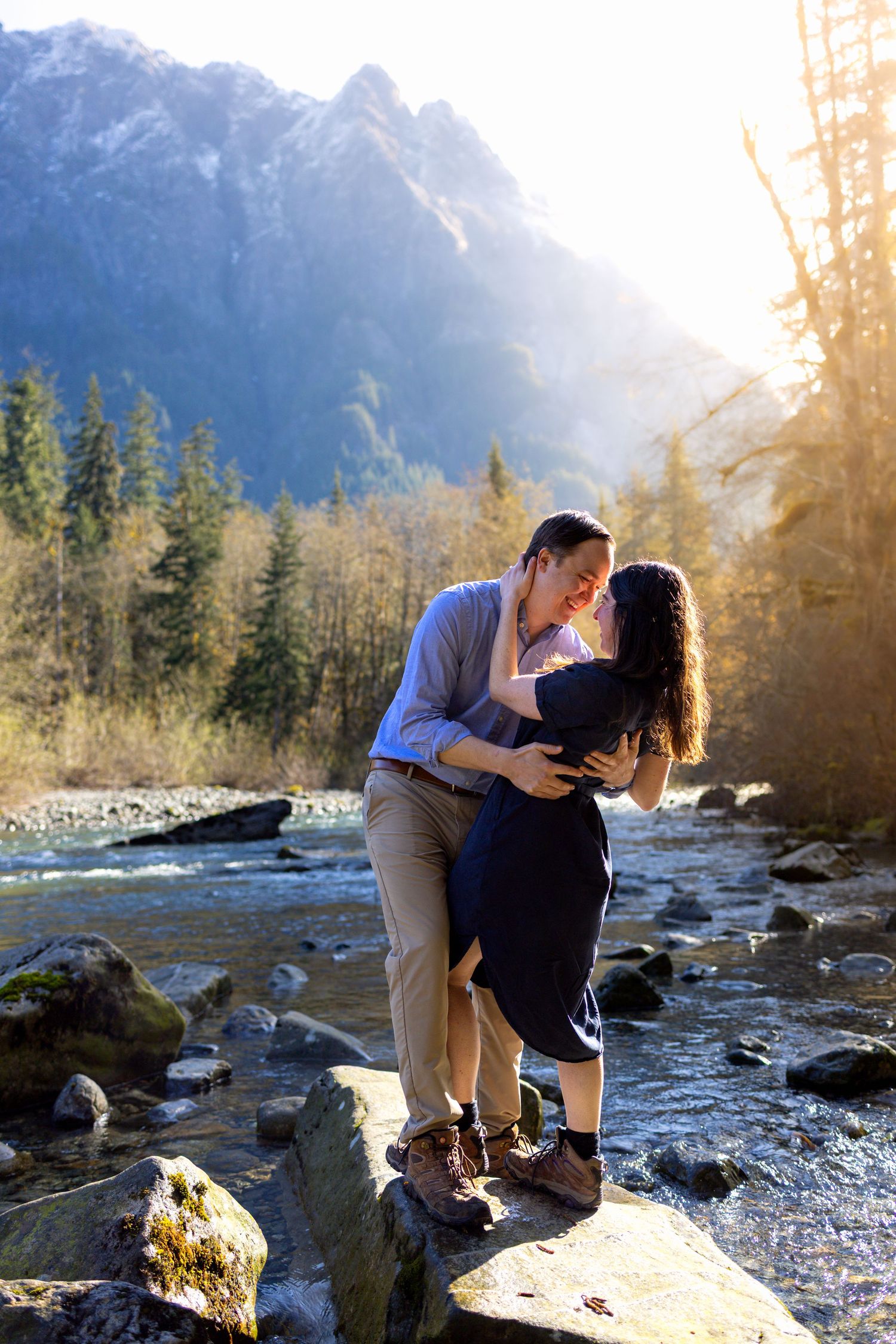 A couple shares a romantic moment on rocks by a mountain stream at sunset.