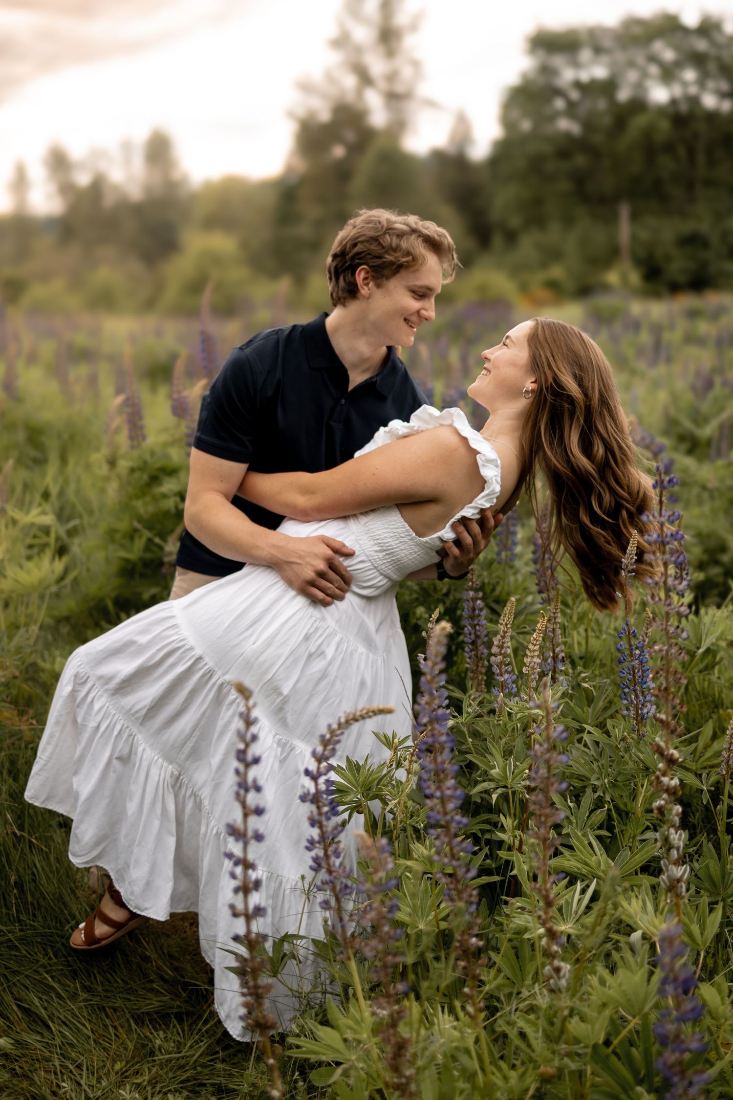 Dancing couple in white dress and black shirt among blooming lupine flowers.