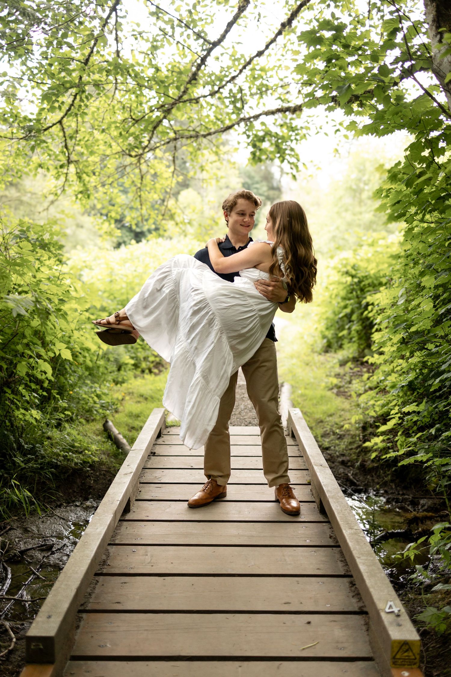 Romantic couple sharing intimate moment on wooden bridge in lush forest setting.