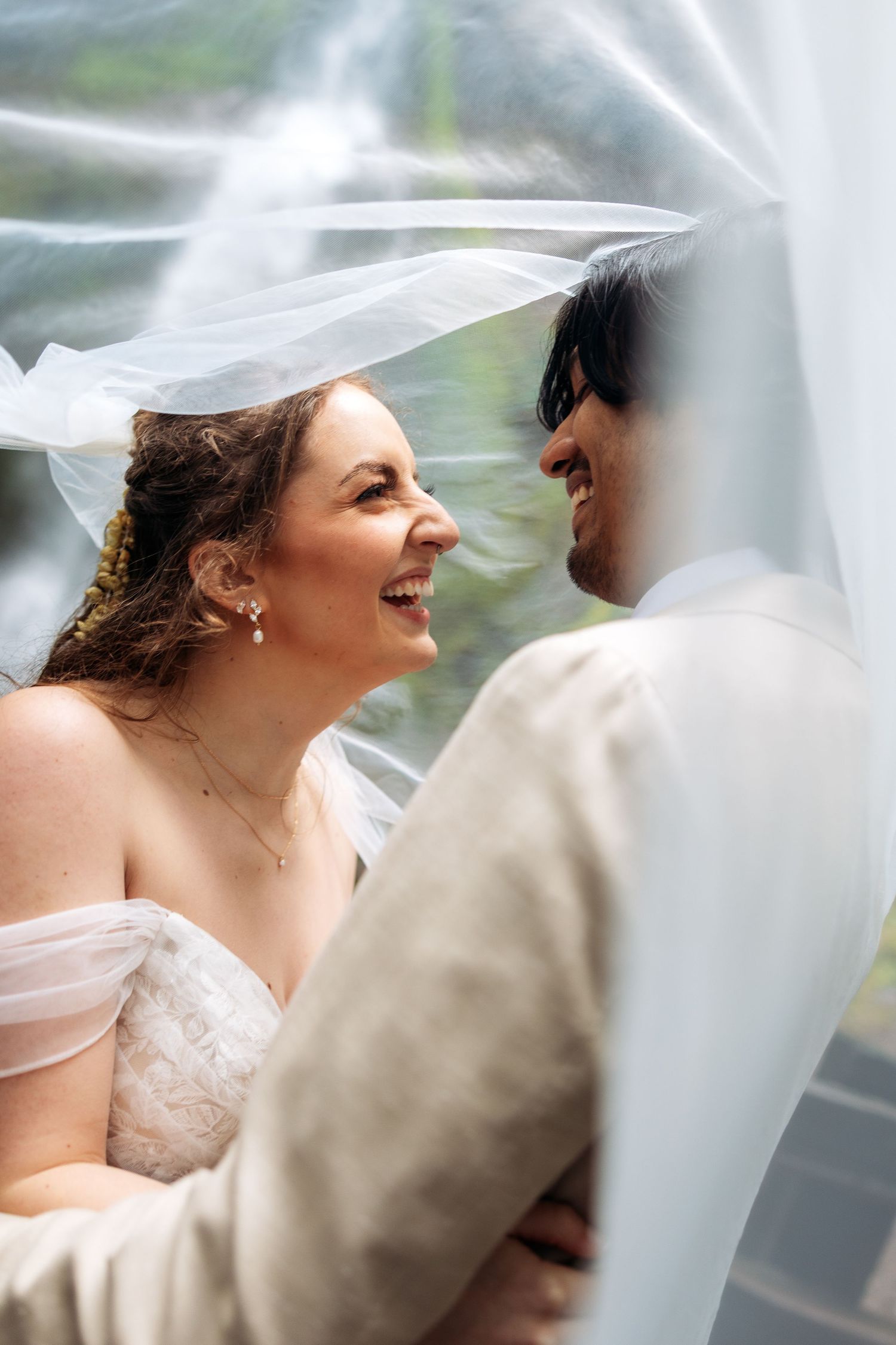 A joyful bride and groom share a romantic moment under a flowing white veil on their wedding day.