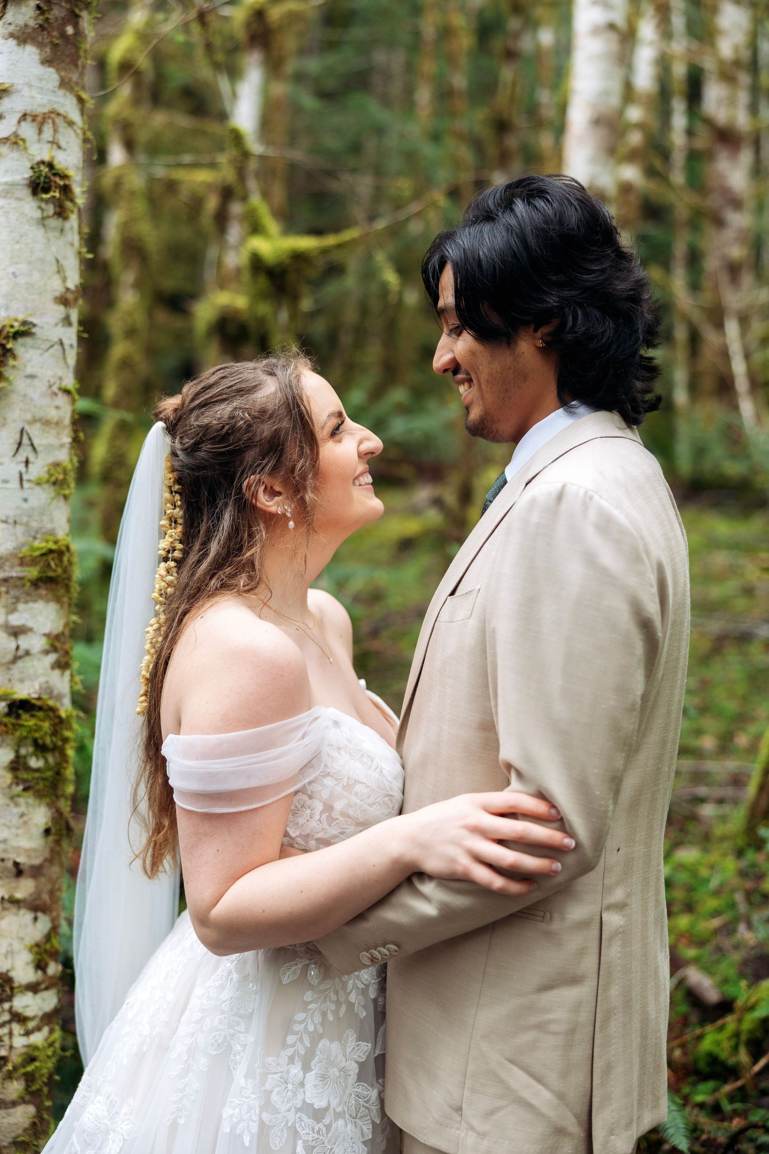 A couple shares a romantic moment in a lush forest setting wearing wedding attire.