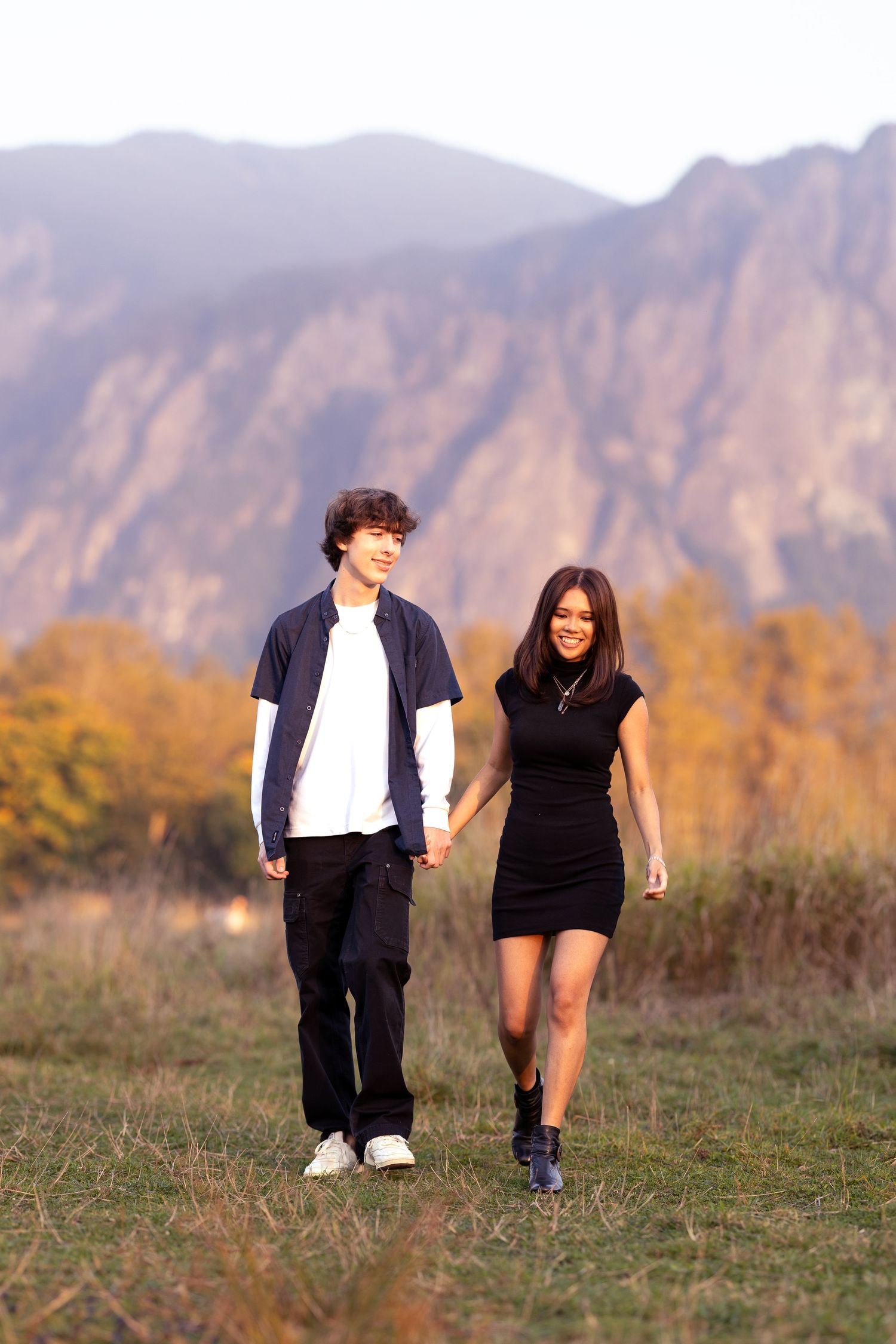Couple walking together on a trail with dramatic mountain backdrop at sunset.