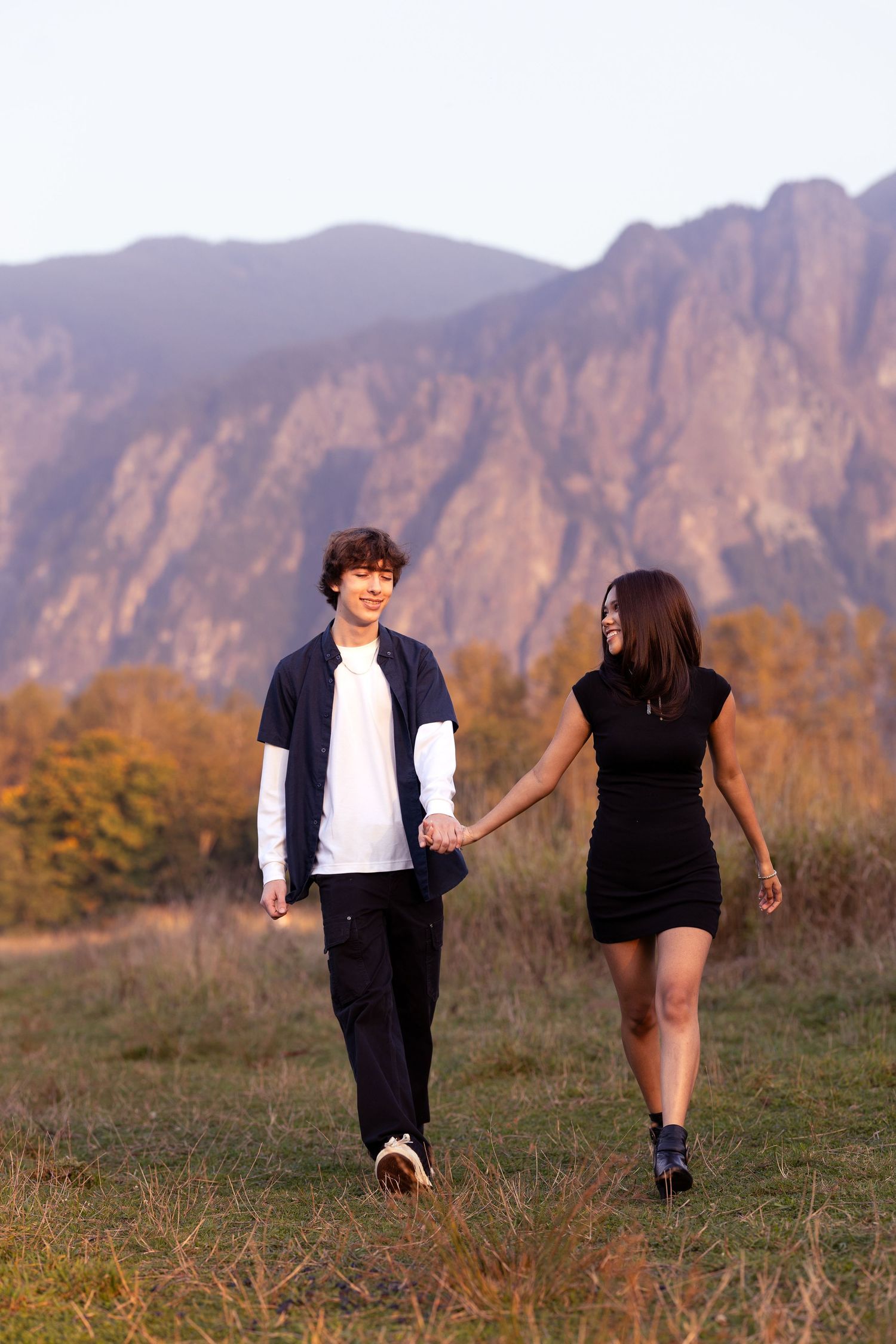 Couple holding hands while walking through mountain meadow at sunset.