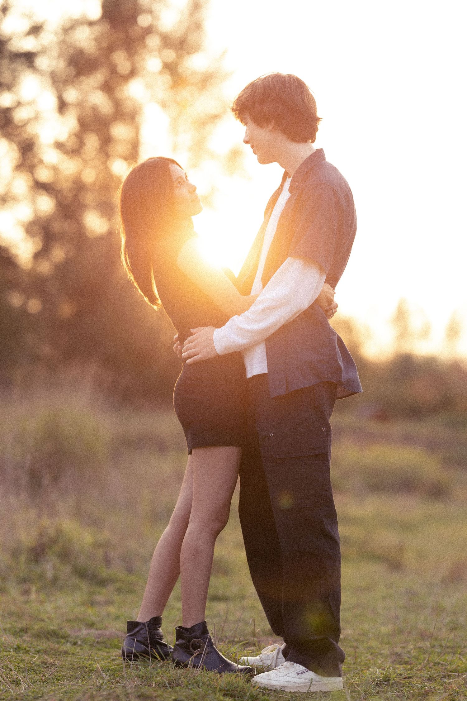 Romantic couple standing close together with golden sunset light behind them.