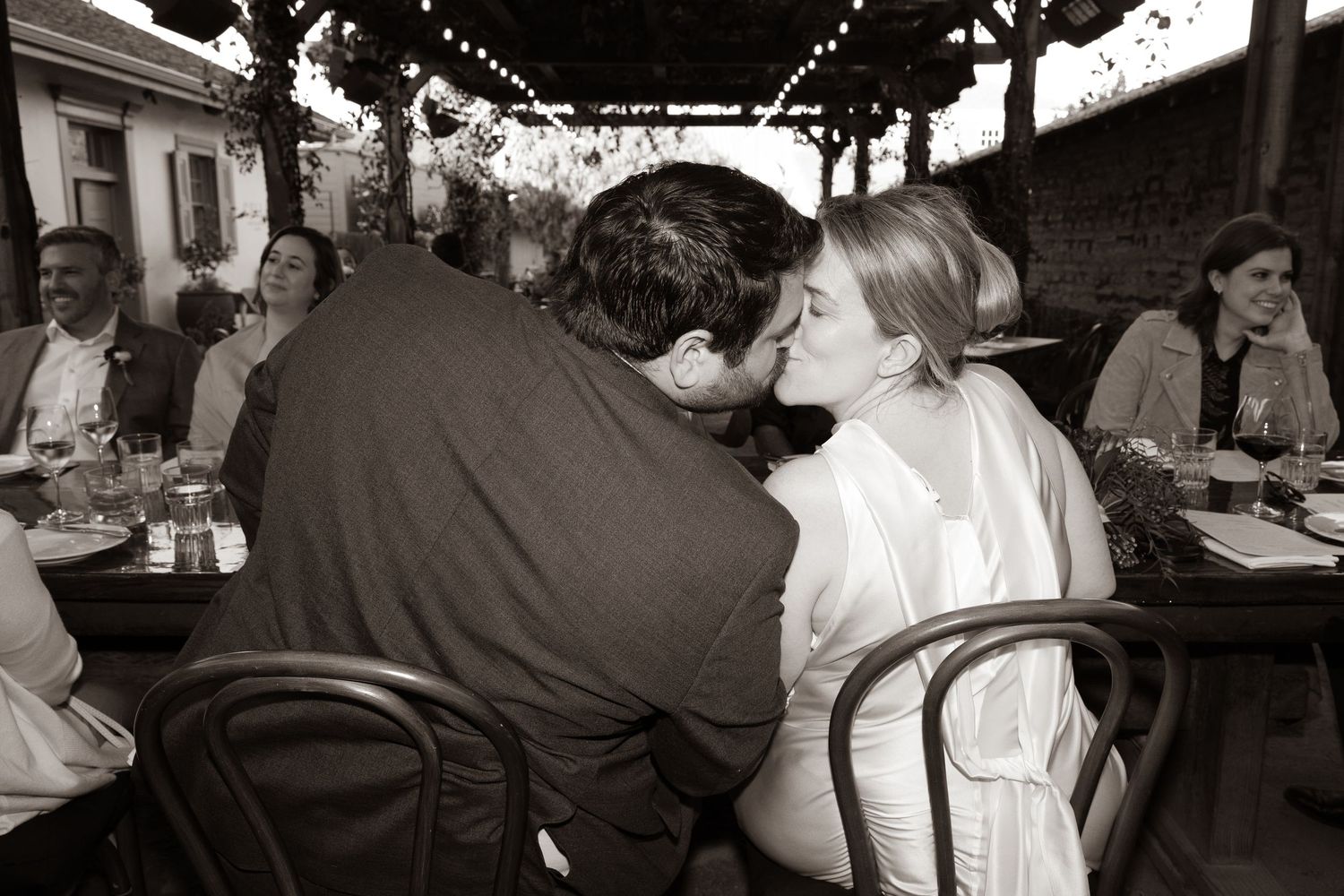 A couple shares an intimate moment at an outdoor cafe with string lights overhead.