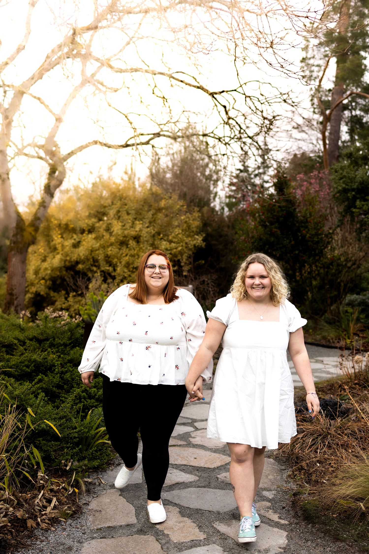 Two people walking and laughing together on a stone path surrounded by greenery.