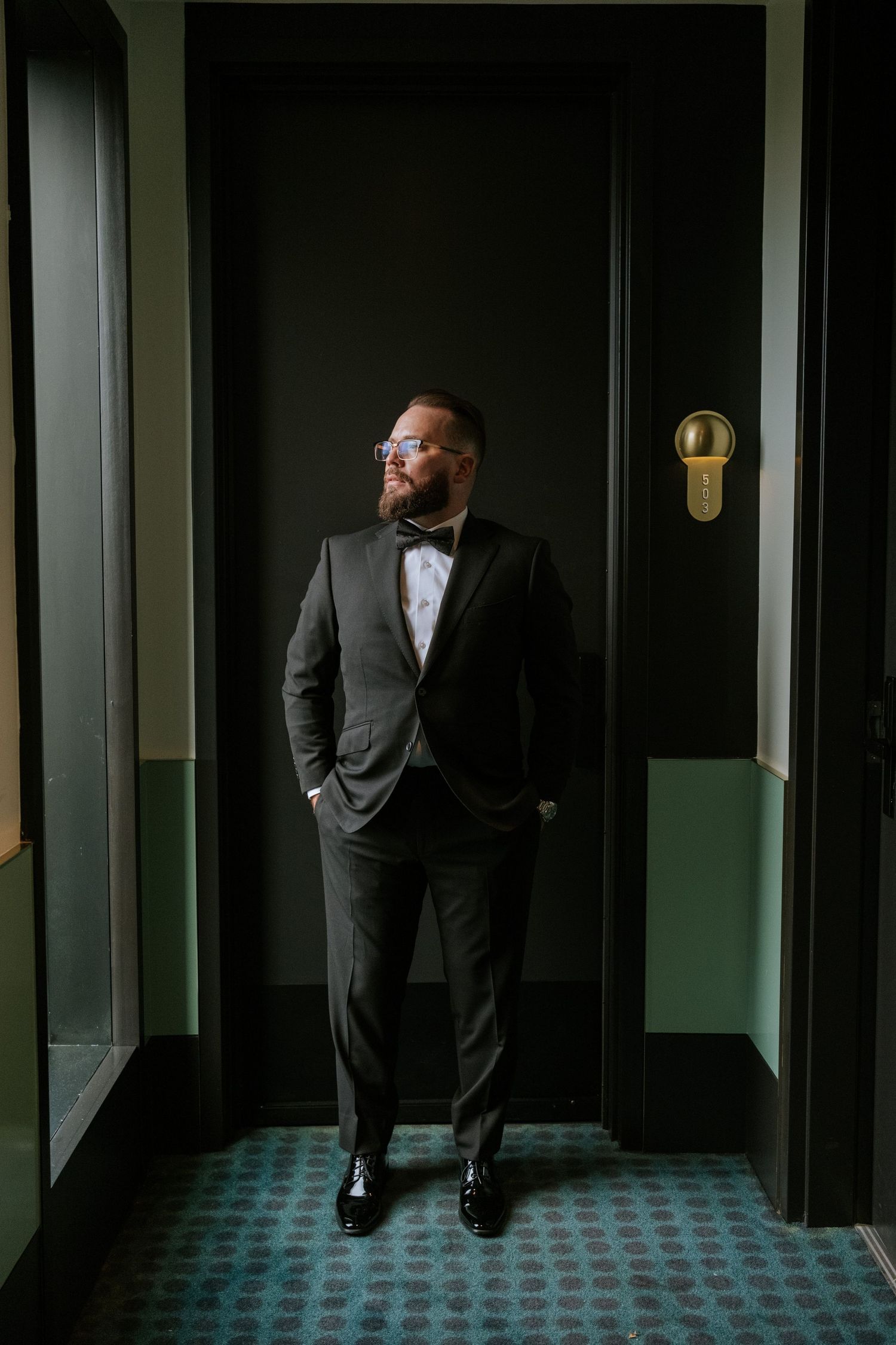 Formal portrait in tuxedo against dark green and black hallway.