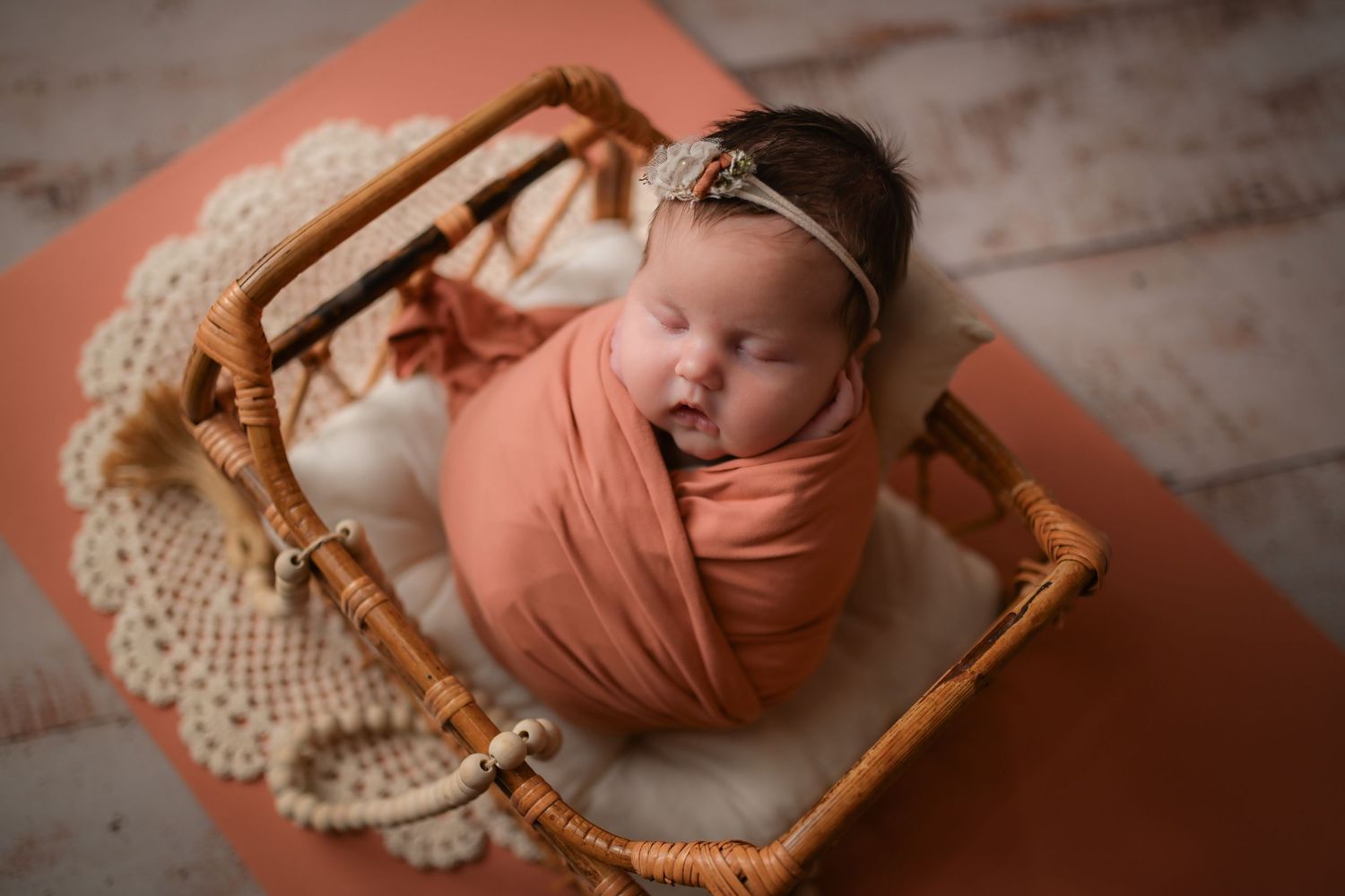 Newborn photography setup with peach tones and vintage wooden prop on textured backdrop.