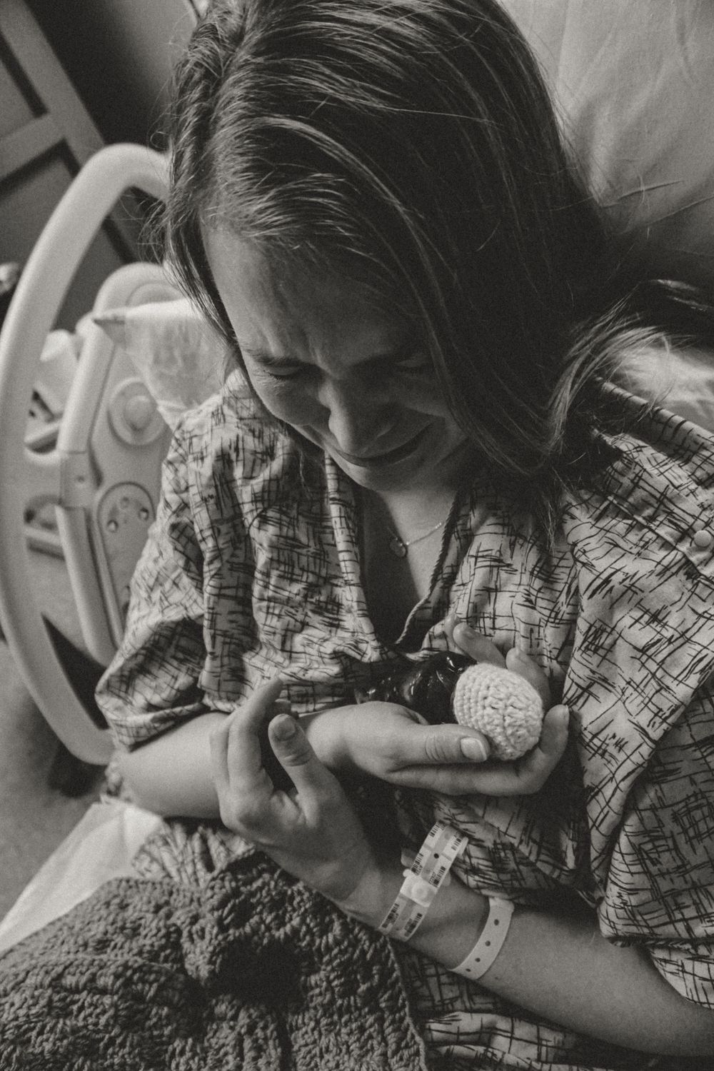 Black and white photo of someone in a patterned shirt looking down at their hands in a tender moment of care.