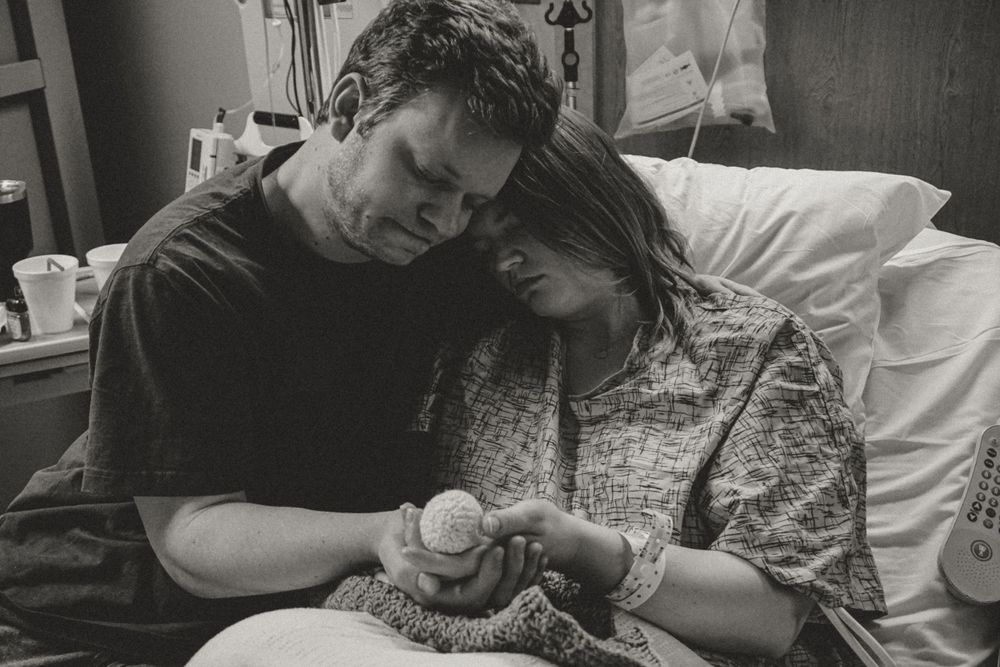 A couple in a hospital room shares an intimate moment while holding a newborn baby.