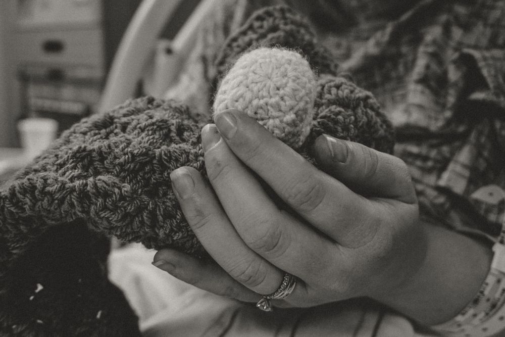 Black and white image of hands holding both knitted fabric and a ball of yarn while crafting.
