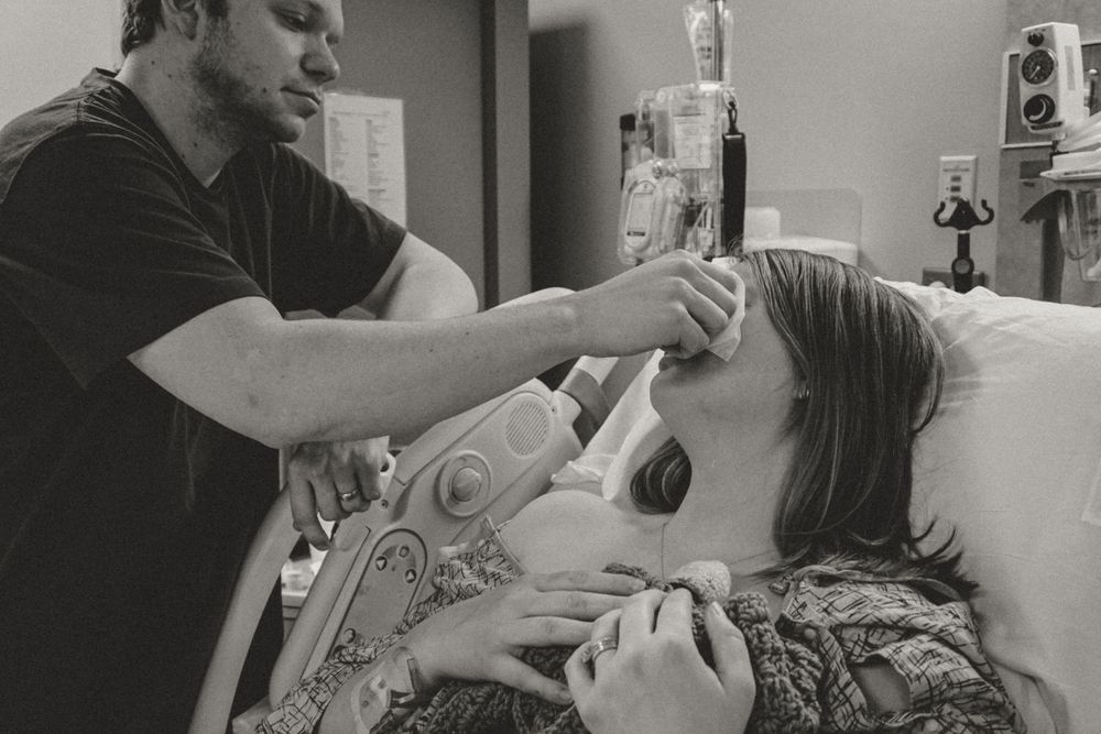A black and white photograph shows someone receiving medical care while lying in a hospital bed.
