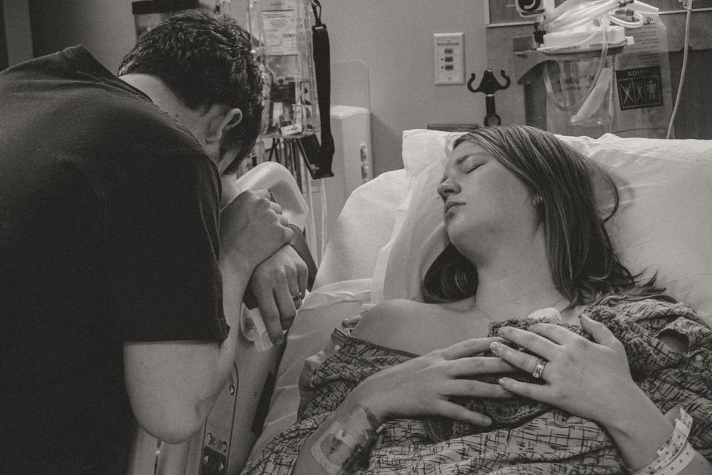 A couple sharing an intimate moment in a hospital room with medical equipment visible in the background.