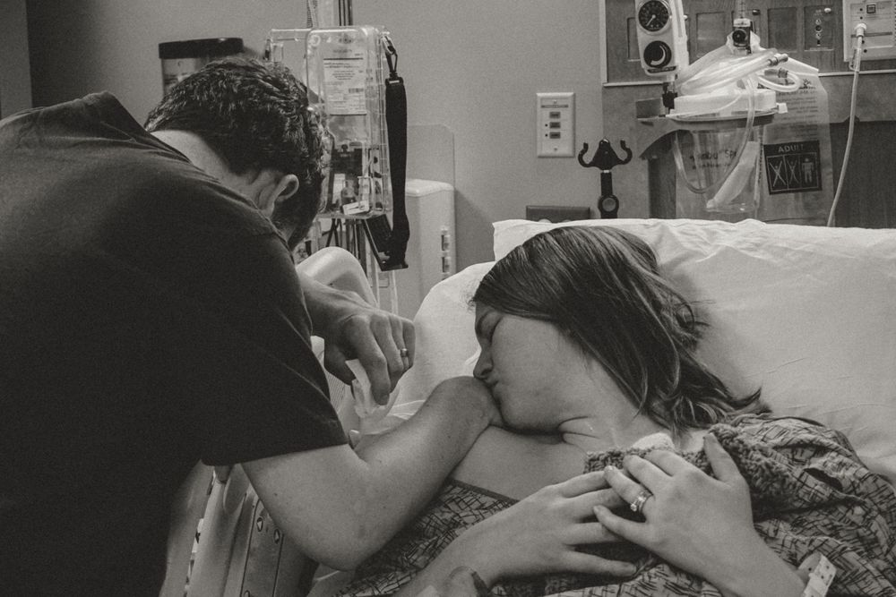 A monochrome photo showing an emotional moment at a hospital bedside as someone comforts a patient.
