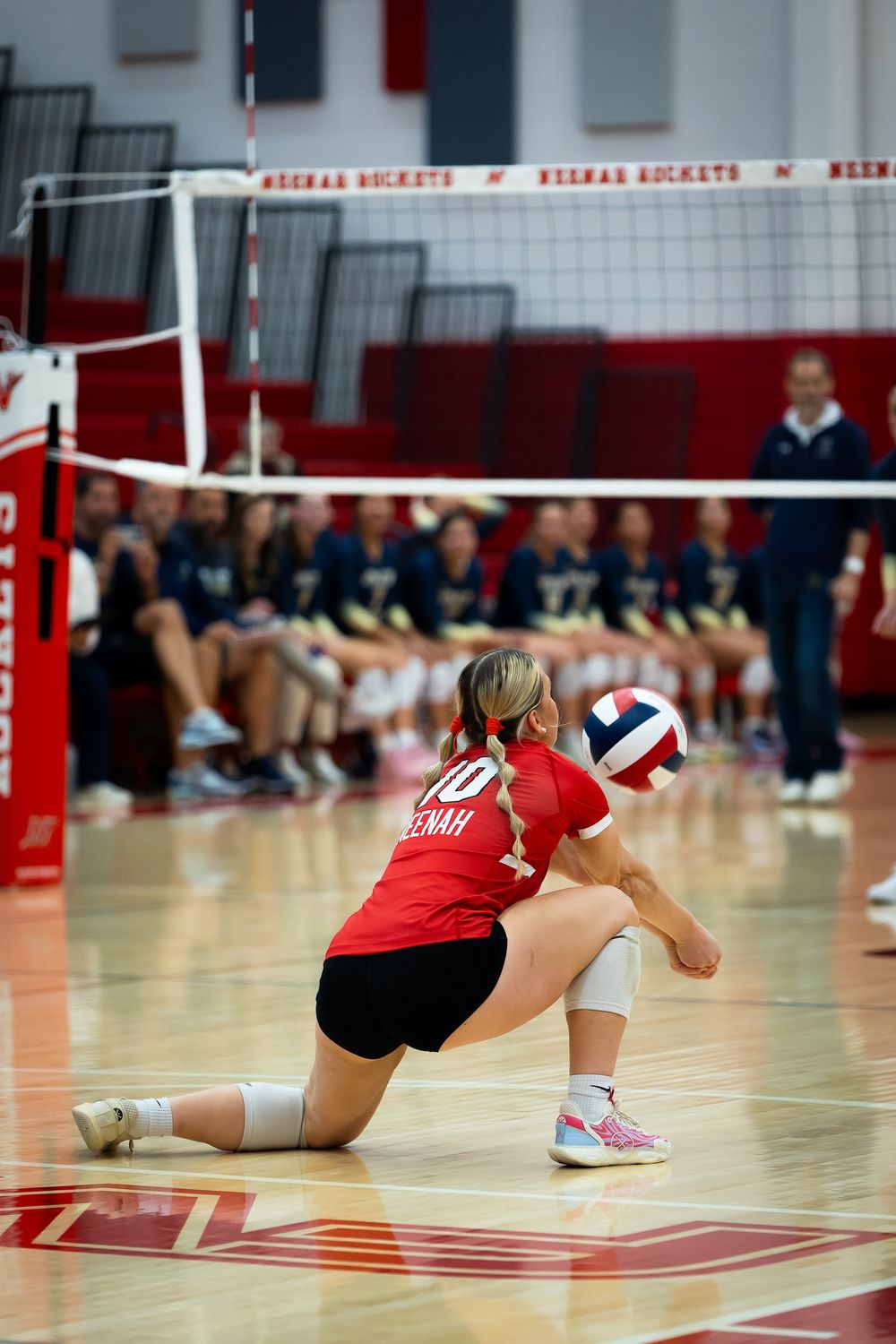 Player in red jersey digs for volleyball during competitive match.