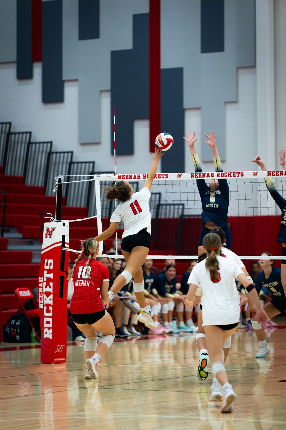 Player leaps high to spike volleyball over net during intense game action.