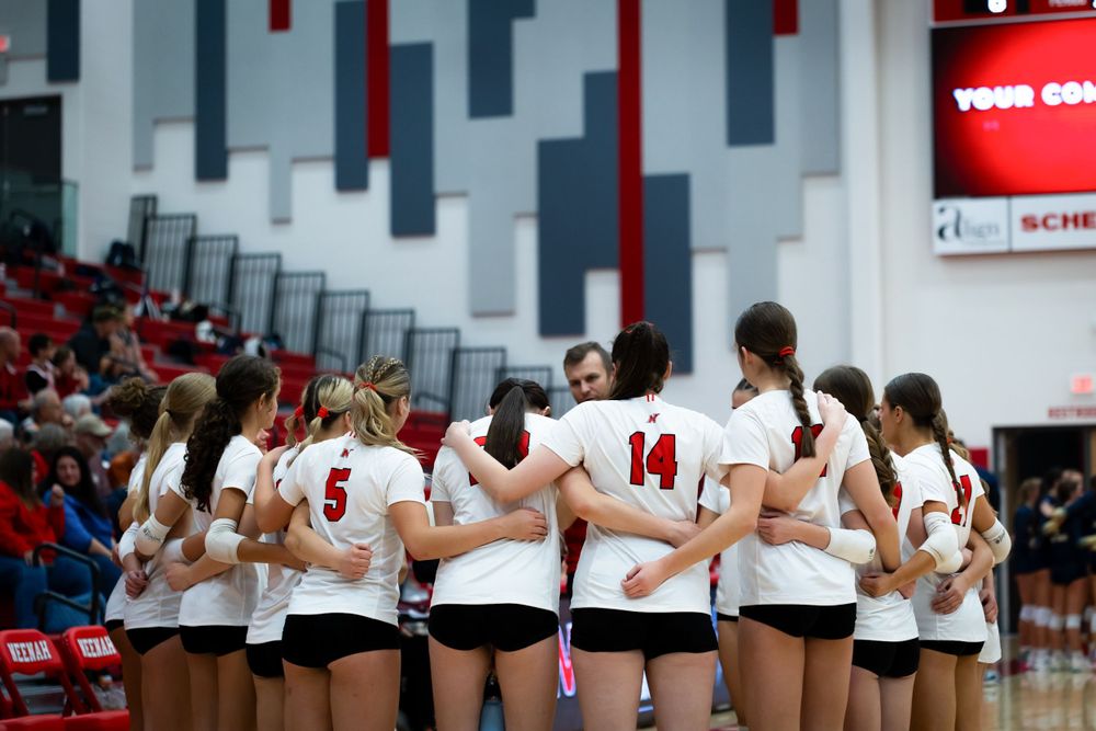 Team stands together arm-in-arm during volleyball match in gymnasium.