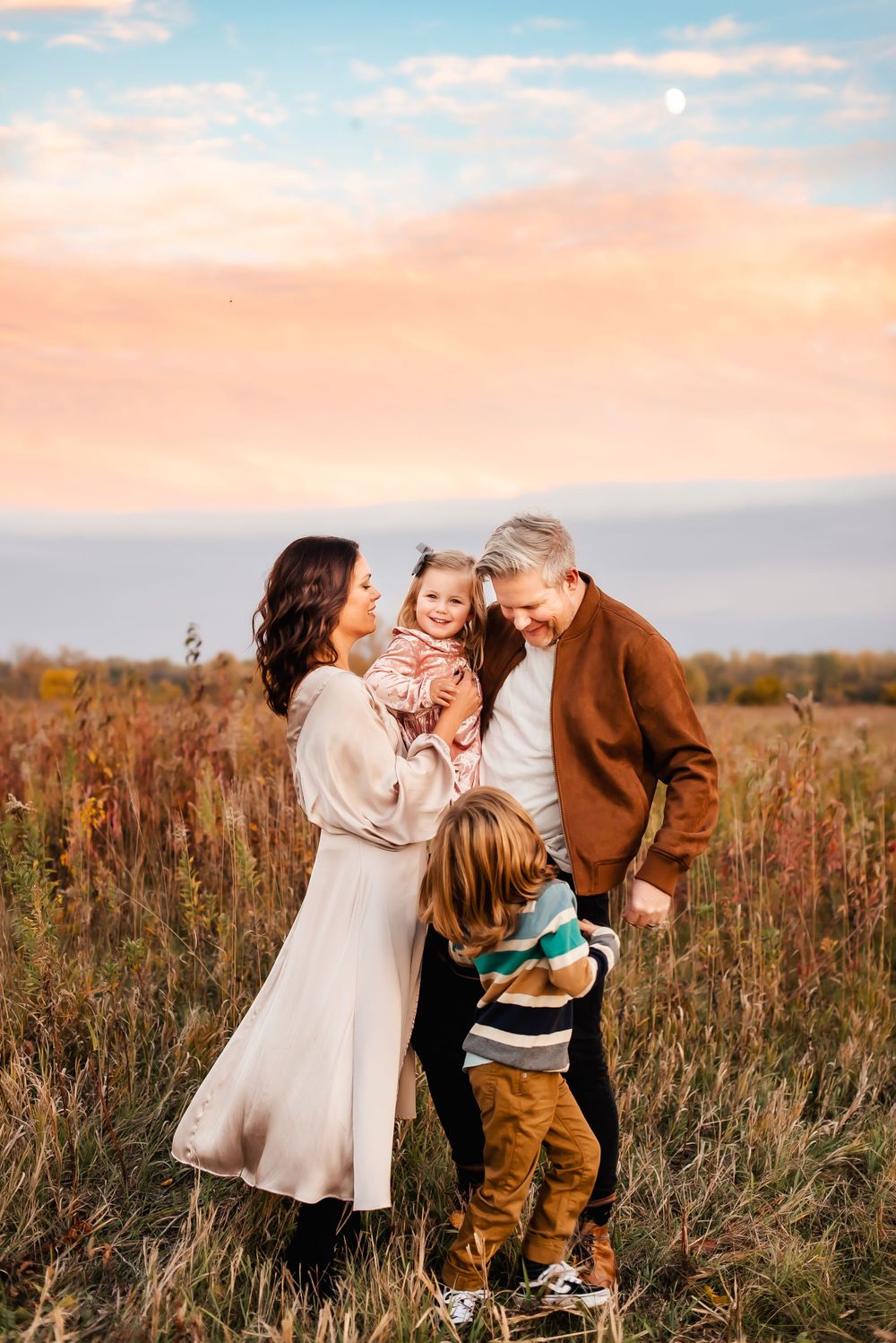 A tender family moment captured at sunset in a golden field with warm autumn colors and glowing light.