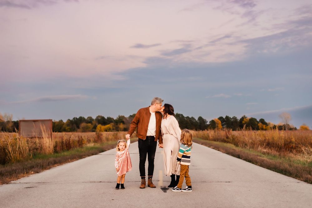 Family walking together on a rural dirt road at sunset with golden light and autumn grass in the background.