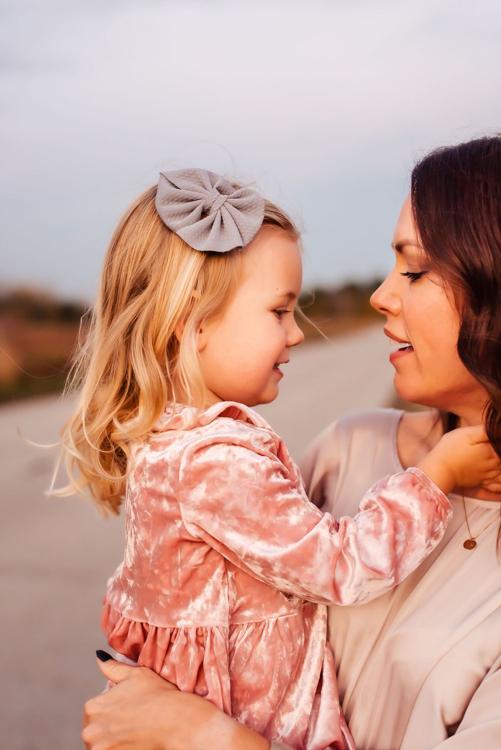 A sweet moment captured at sunset showing affection between parent and child wearing a pink velvet dress and bow.