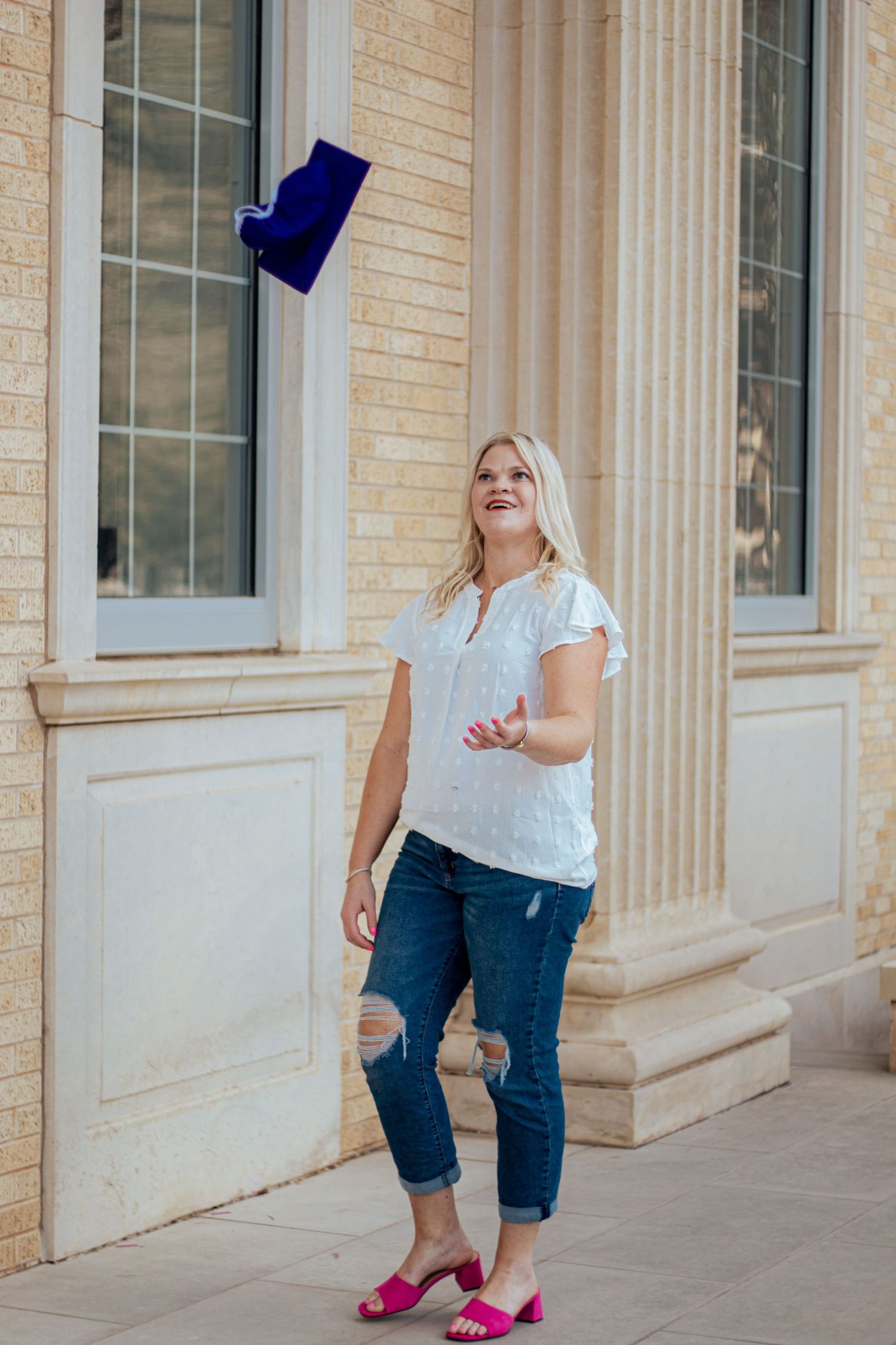A joyful moment captured outside a brick building wearing distressed jeans, white top and pink flats.
