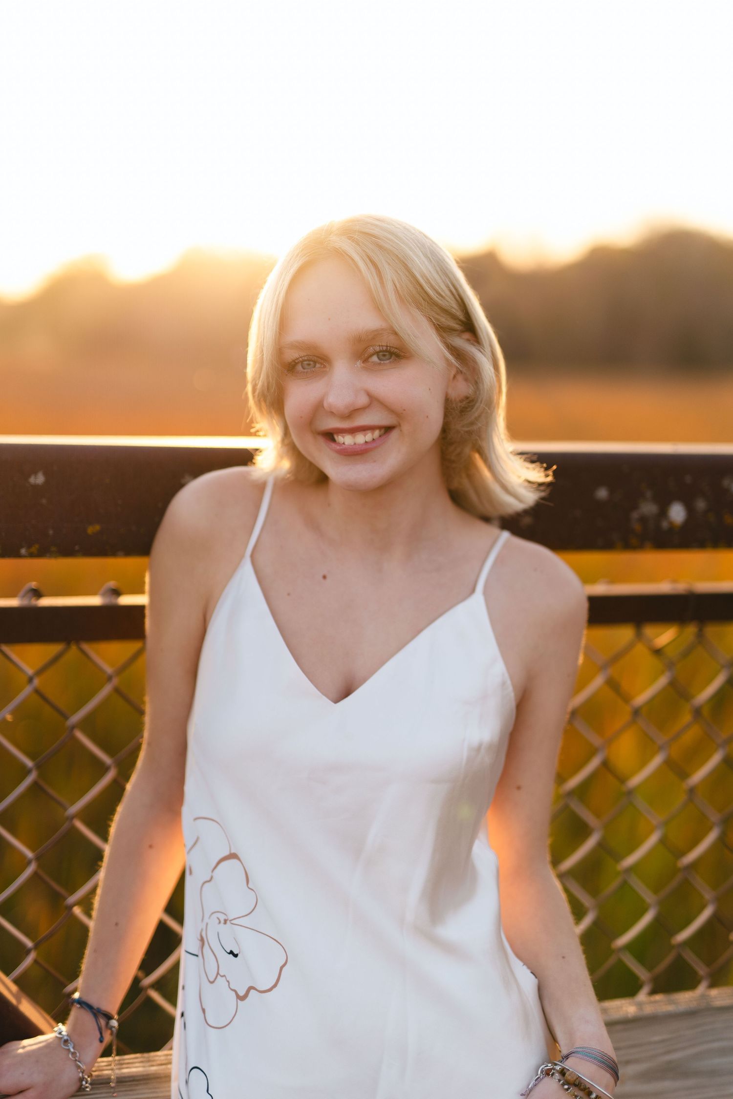 Young woman in white sleeveless top smiling during golden sunset on wooden deck.