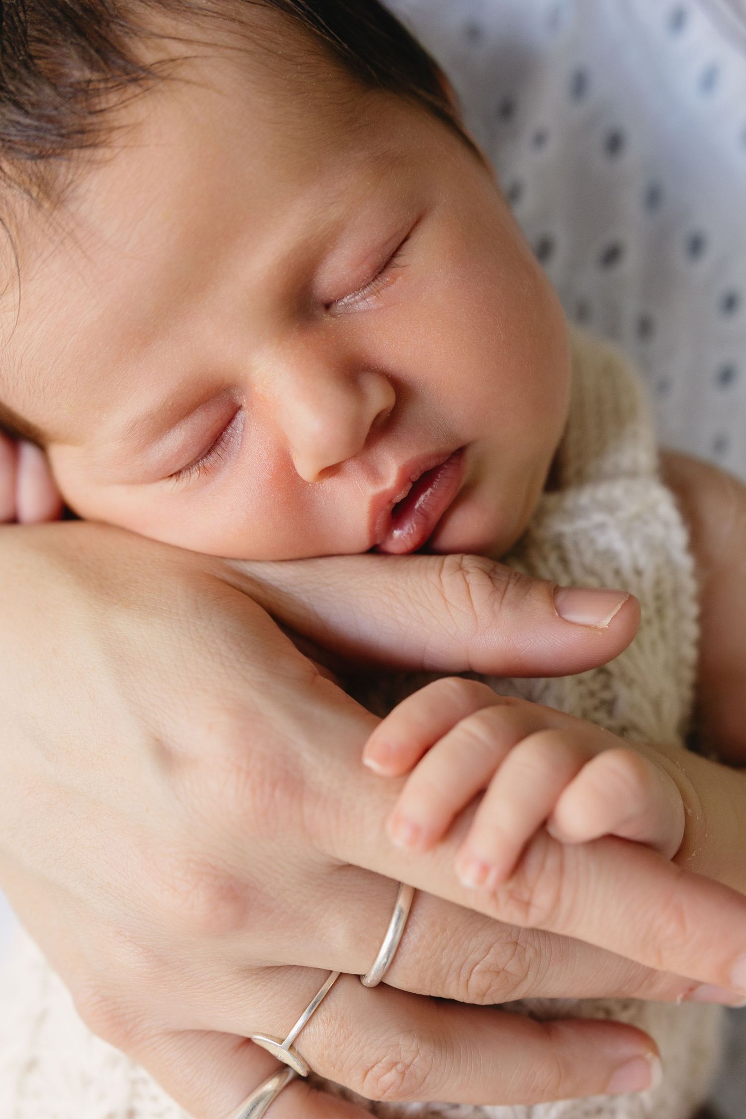 A sleeping newborn baby nestles against a parent in a tender close-up portrait.
