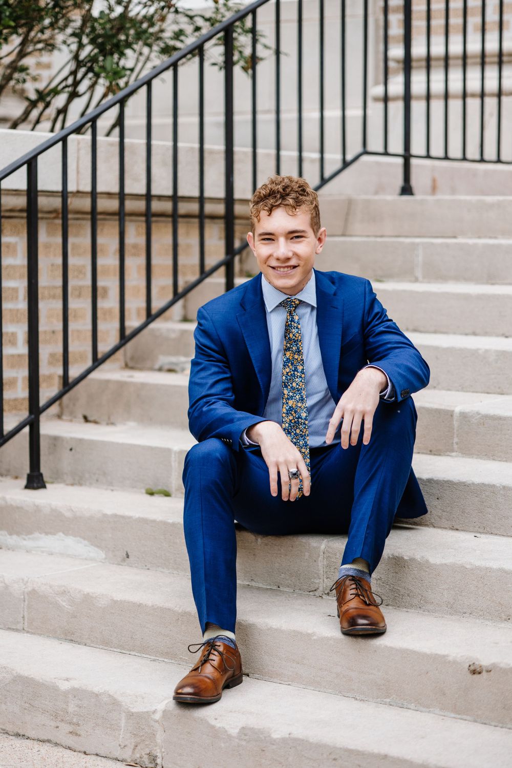 Person in blue suit sits casually on concrete steps with ornate metal railing.