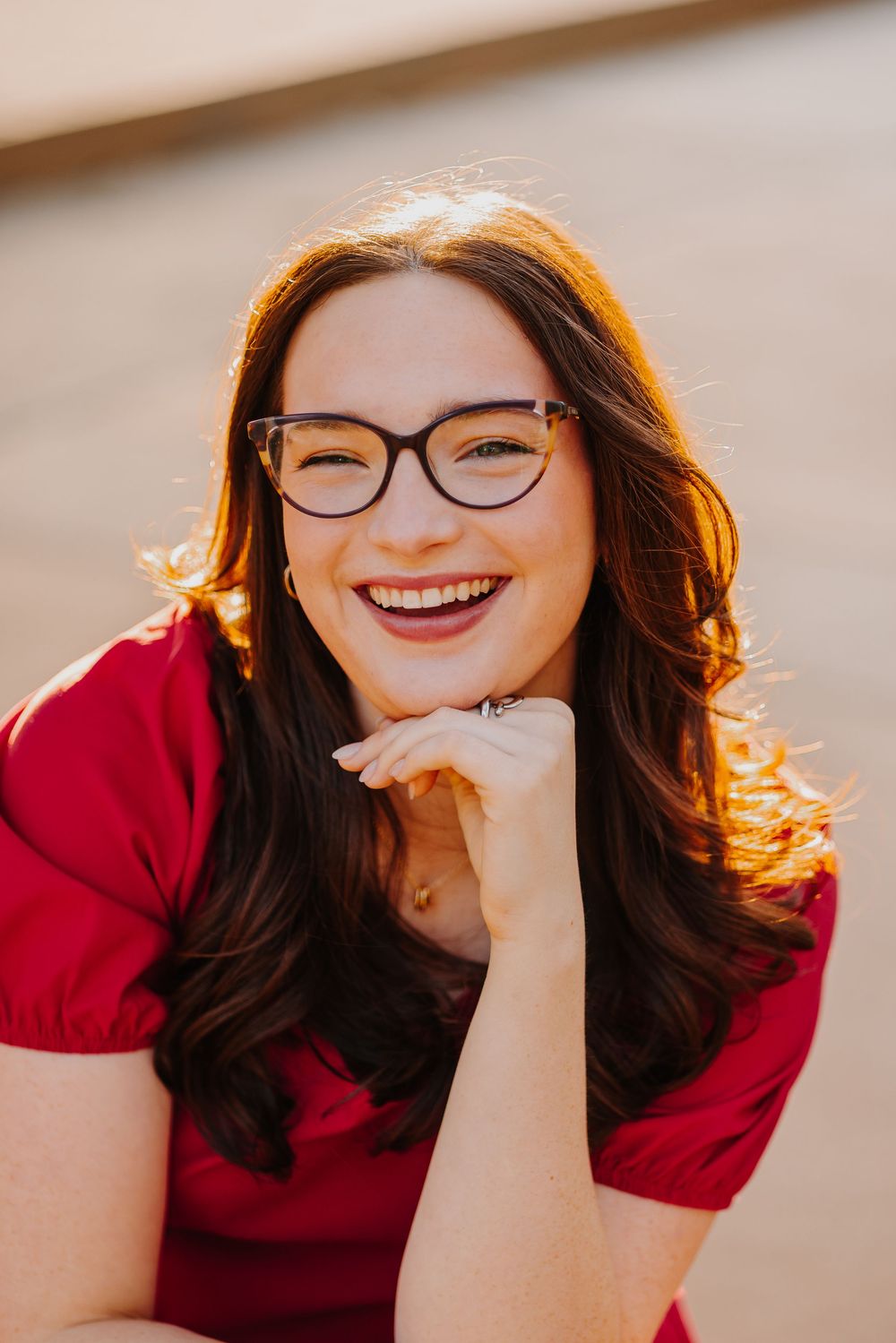 A joyful portrait of someone in a red top and glasses with warm sunlit hair.