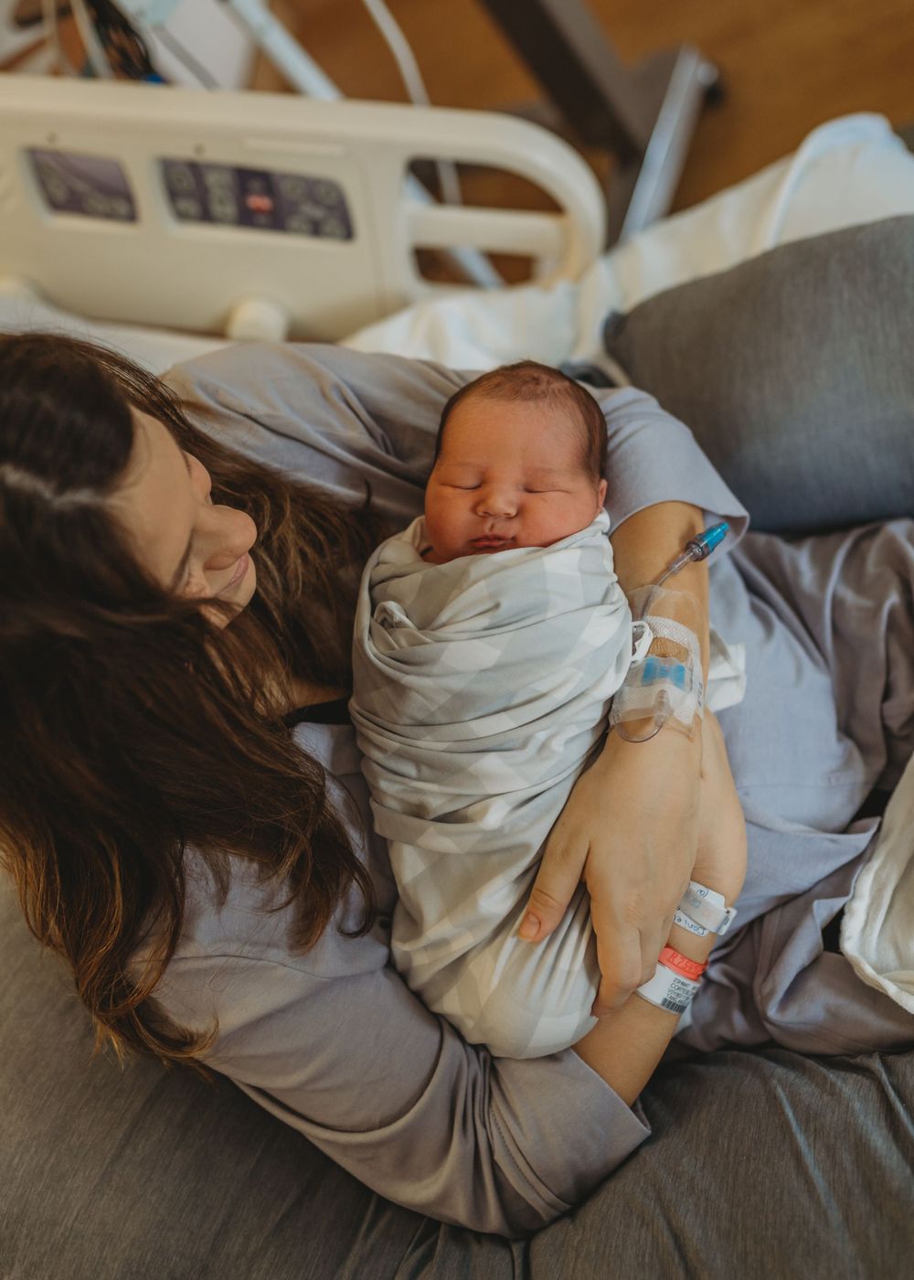 Tender moment in hospital room with newborn swaddled in white.