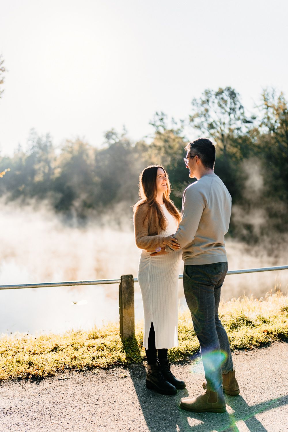 Romantic couple embracing by wooden fence in misty morning sunlight.