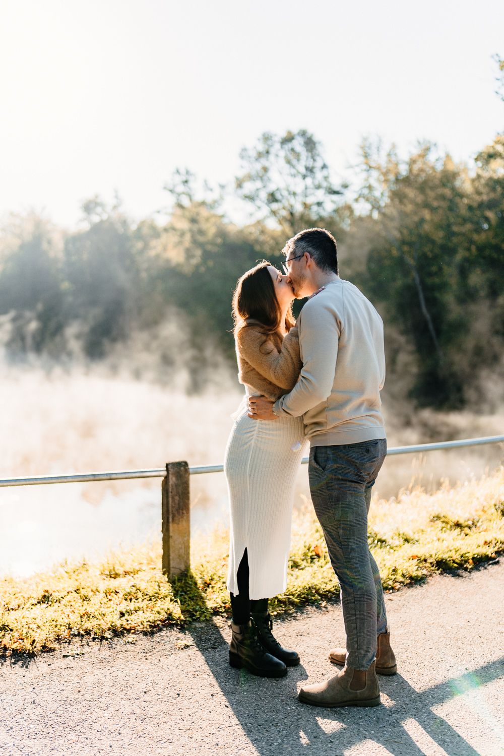 Romantic couple embracing on a misty morning by a wooden railing overlooking water.