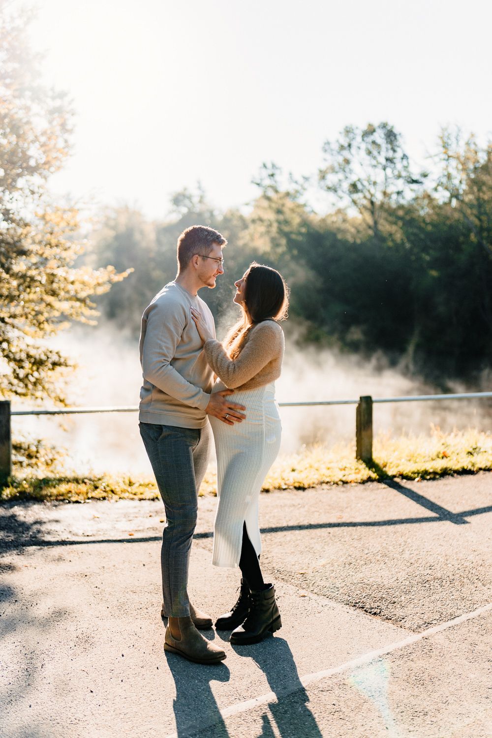 Couple sharing a tender moment on a sunlit path with morning mist rising in the background.