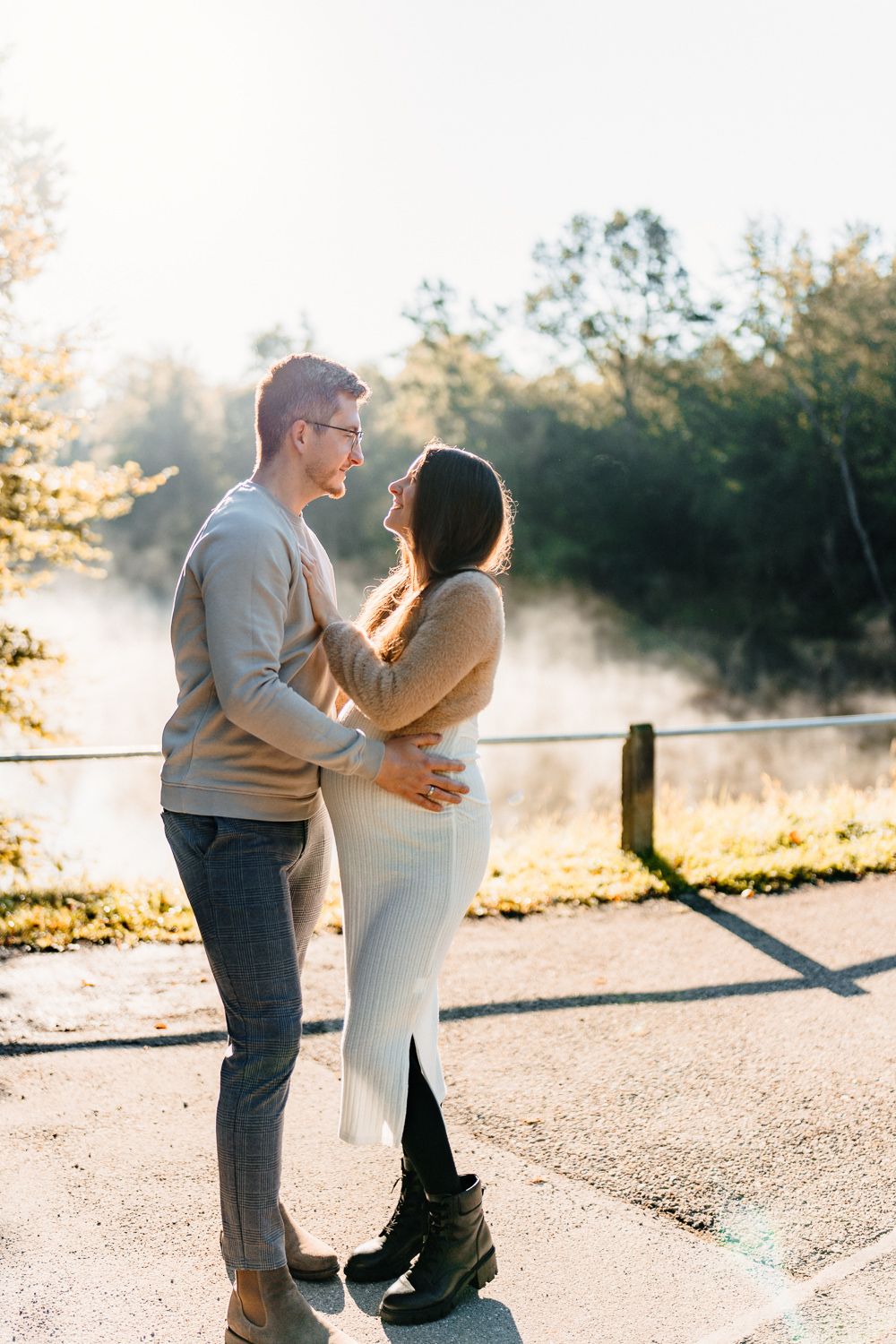 Loving couple embracing on a misty morning path with sunlight streaming through trees.