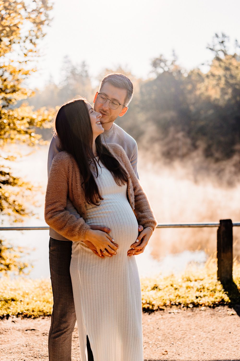 Expecting couple sharing an intimate moment against a backdrop of morning mist and autumn trees.
