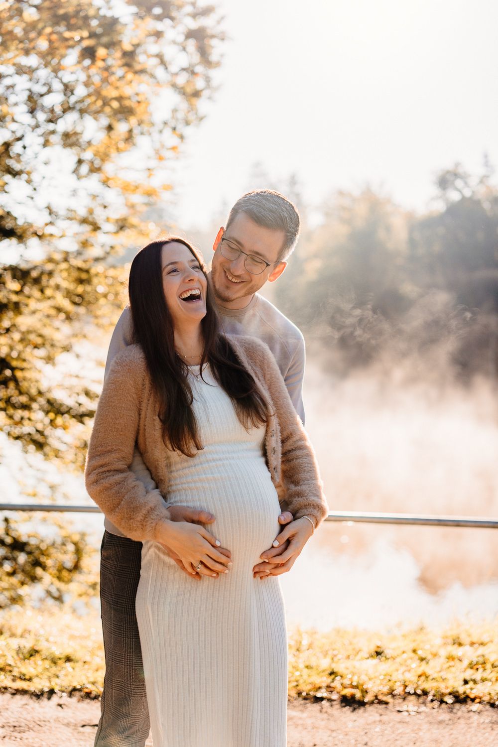 Happy couple laughing together during maternity photoshoot on a misty morning.