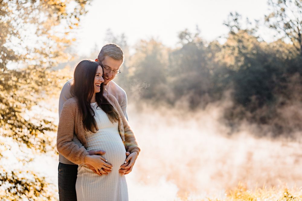 Maternity photo of couple embracing in soft morning light with fog rolling across the landscape.