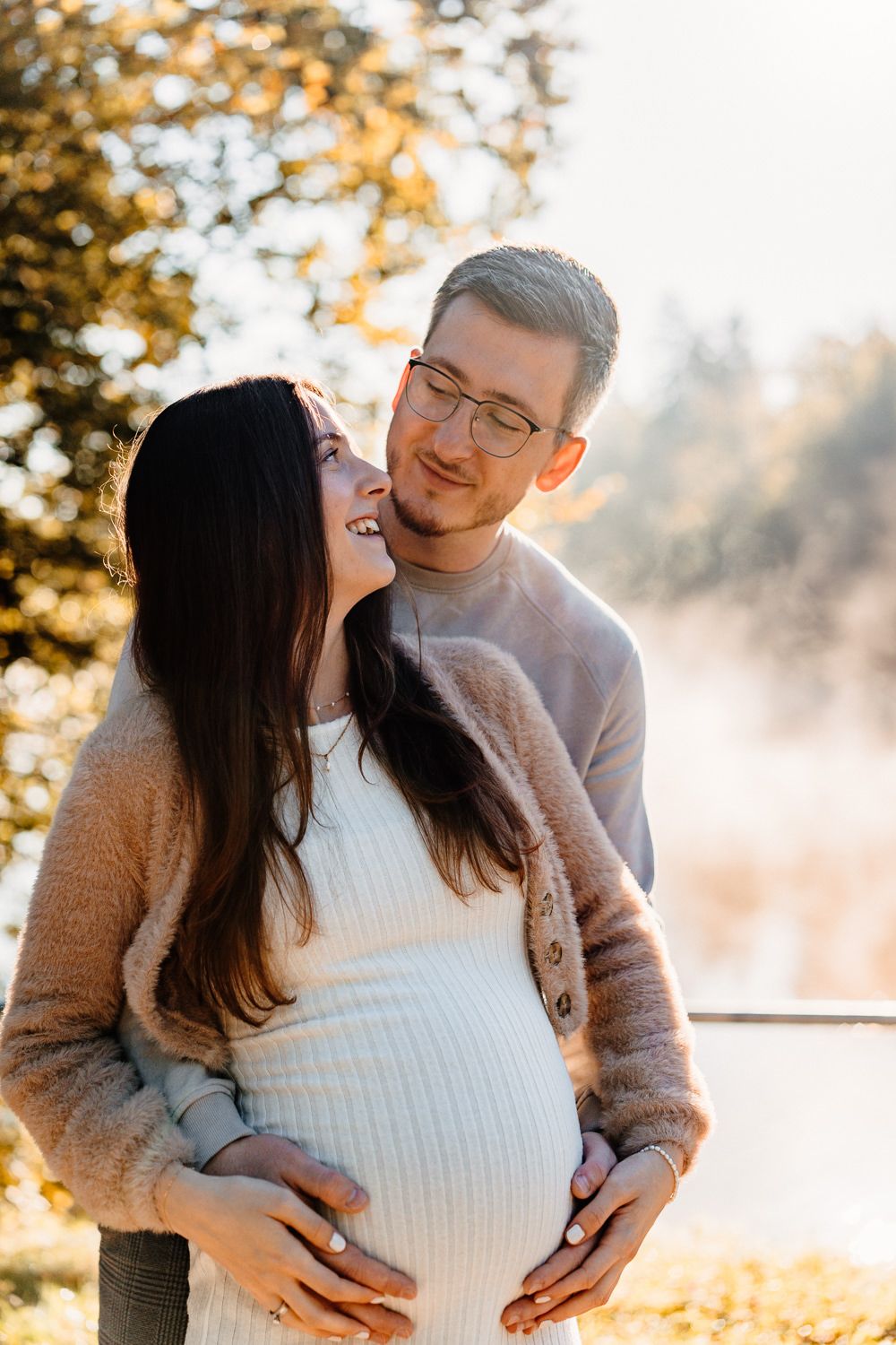 Joyful maternity photo captured in warm autumn light with couple sharing intimate moment.