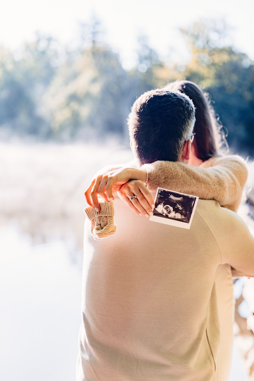 A sonogram photo held up against a beige sweater with misty lake in background.