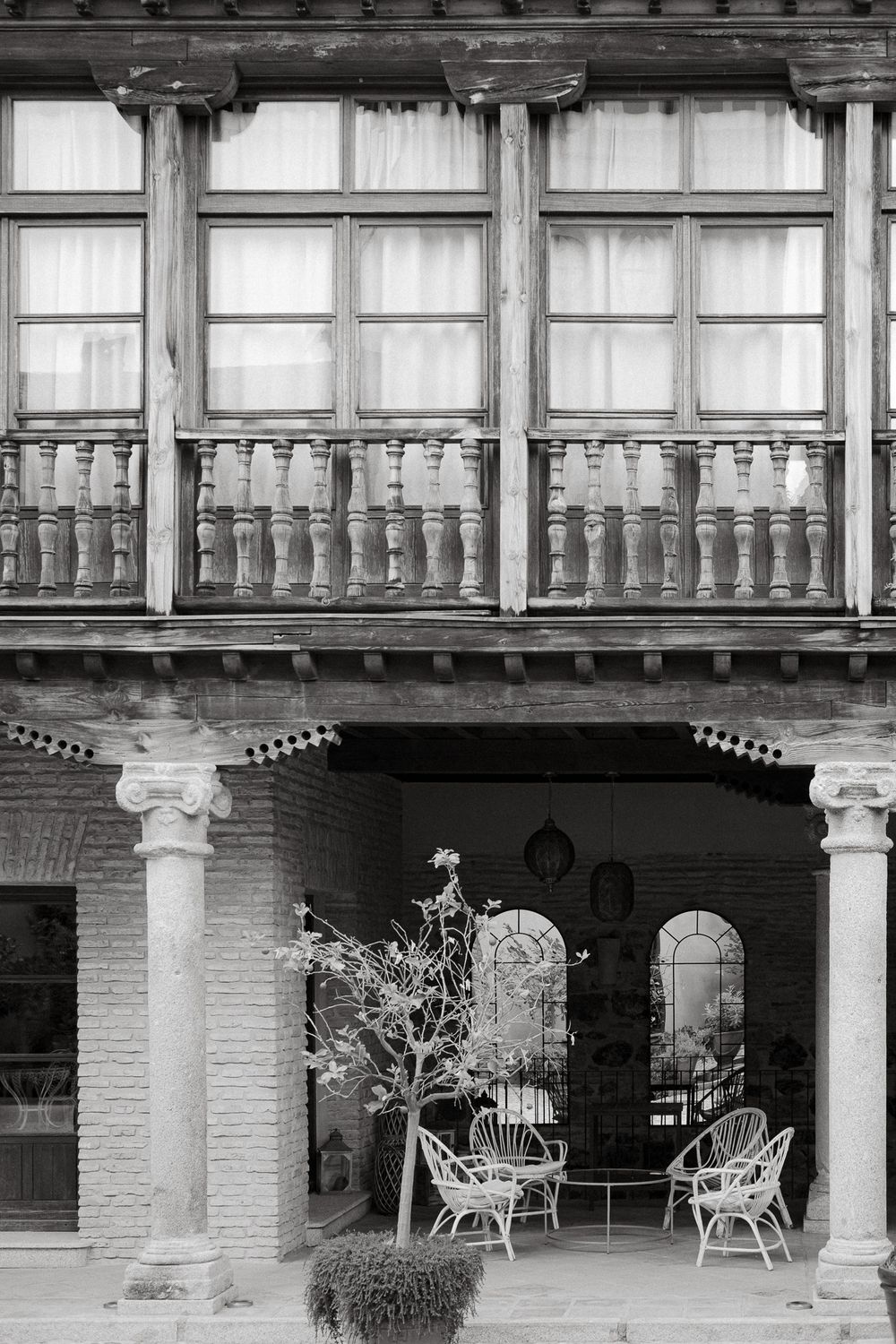 Black and white photo of traditional wooden balcony with columns and outdoor seating area below.