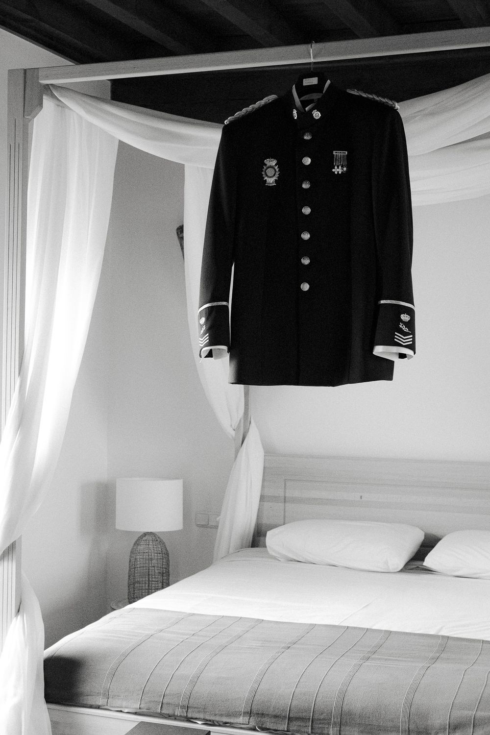 Military dress uniform hanging above a white bed with sheer canopy drapes.