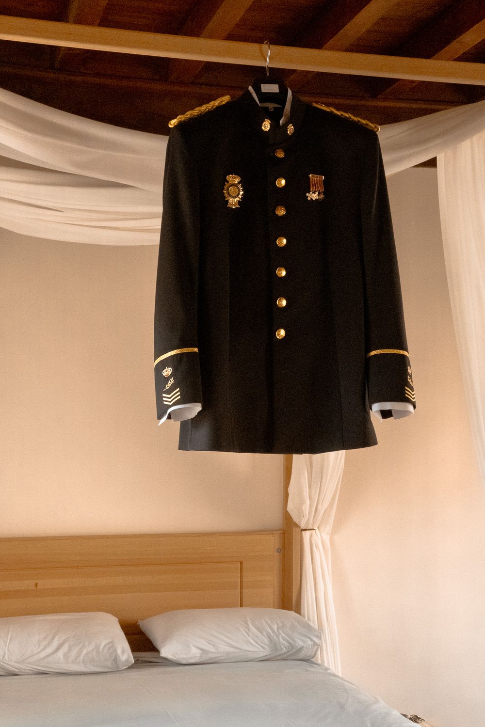 Formal military dress uniform with gold buttons and medals displayed above a canopy bed.