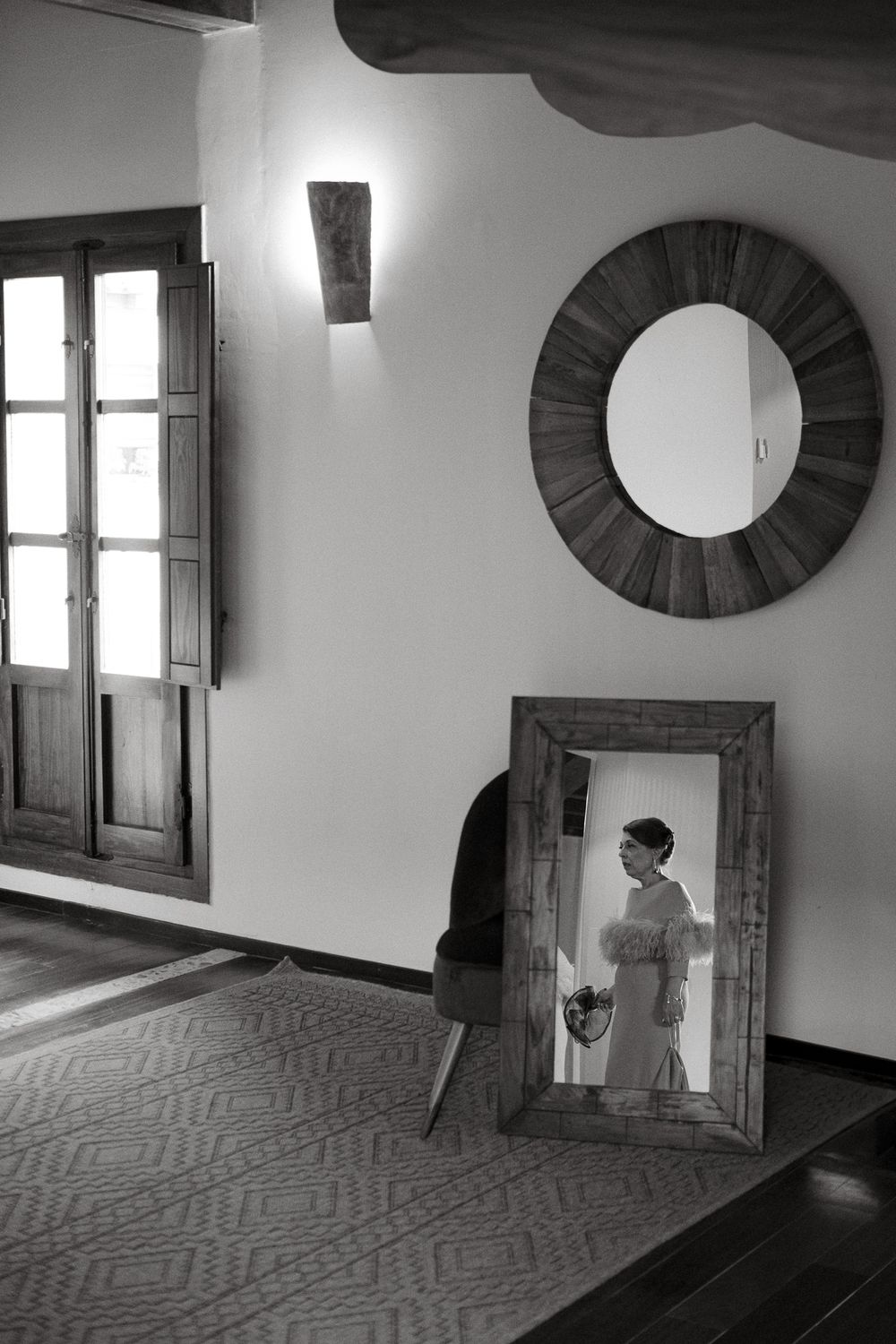 Black and white interior with vintage window, circular mirror, and framed artwork leaning against wall.