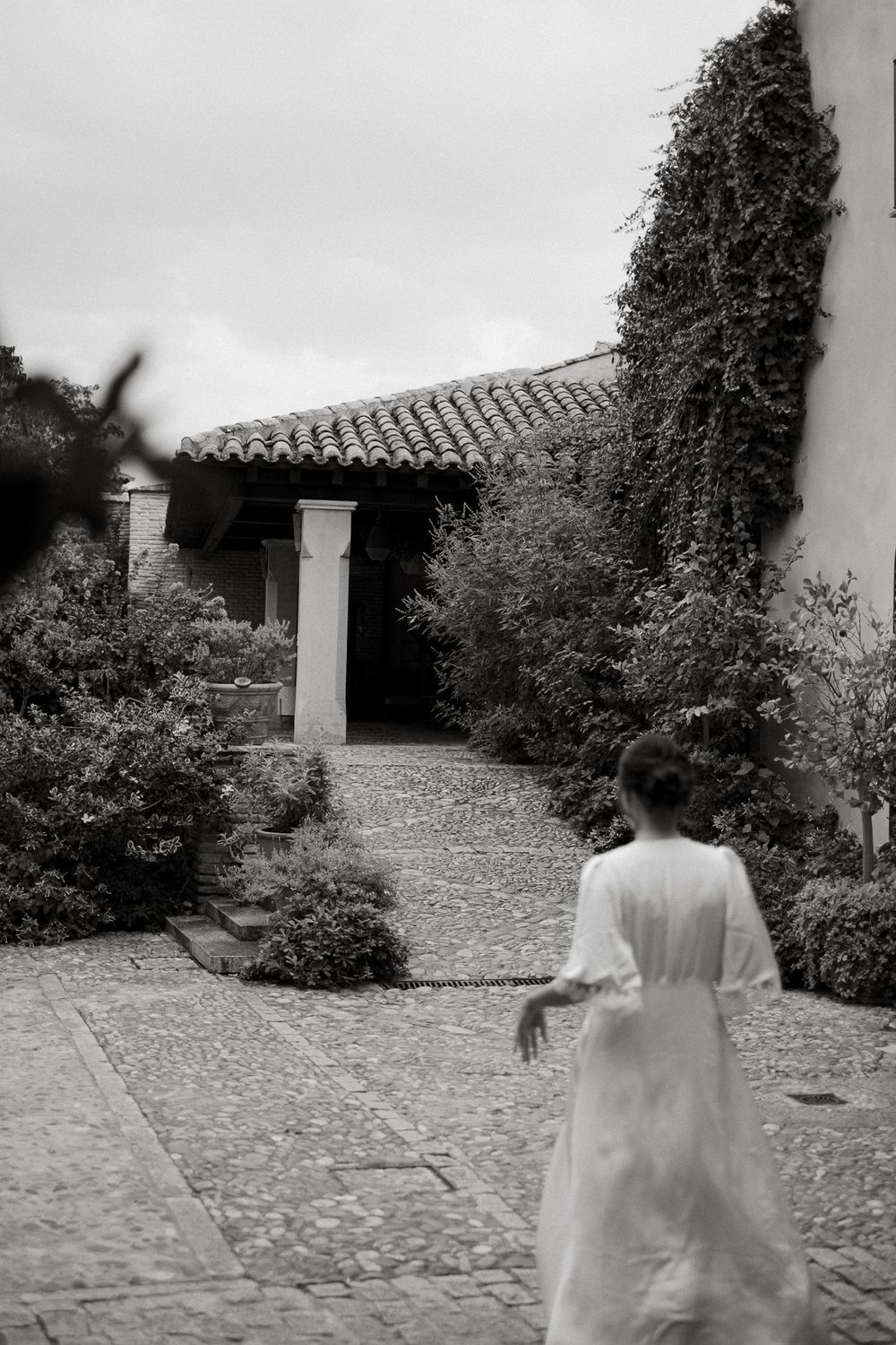 Black and white garden path leading to columned entrance with overgrown vines.