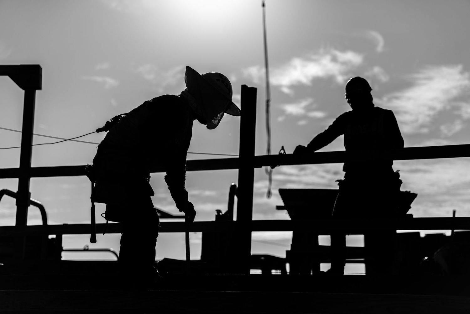 Two silhouetted figures working on what appears to be a boat deck against a cloudy sky at sunset.