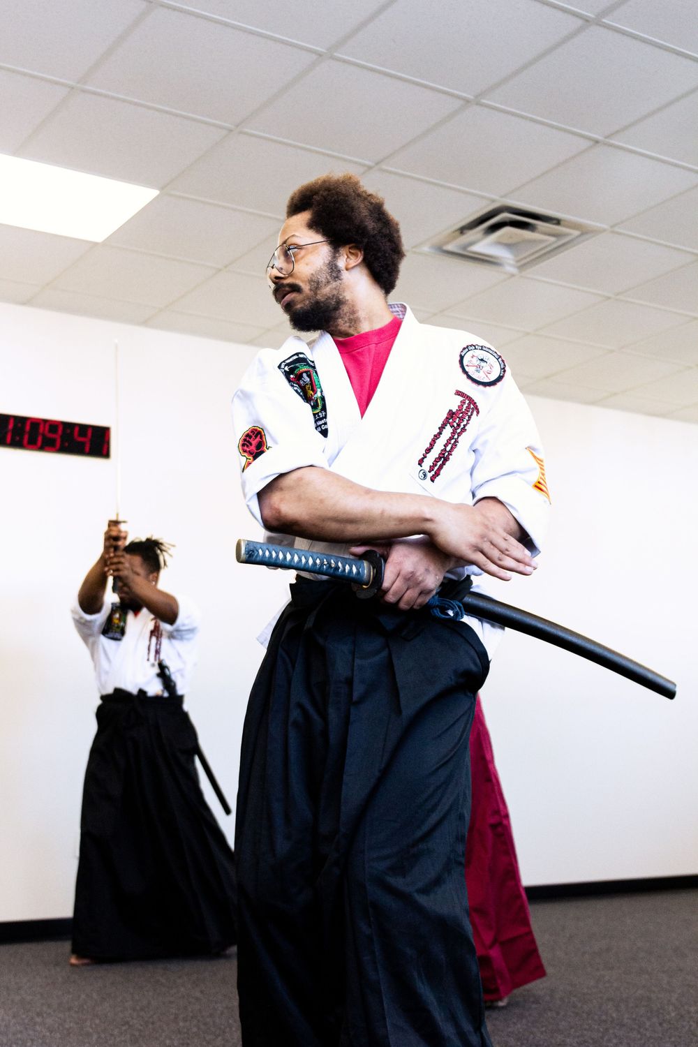Students practicing martial arts movements with katanas in a bright indoor training studio.