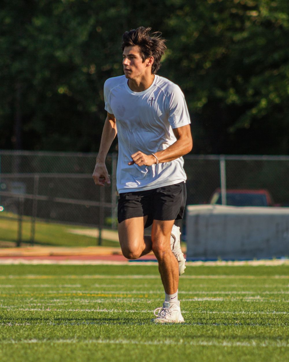 Runner in white t-shirt and black shorts sprinting on a sunny grass field during outdoor frisbee game.